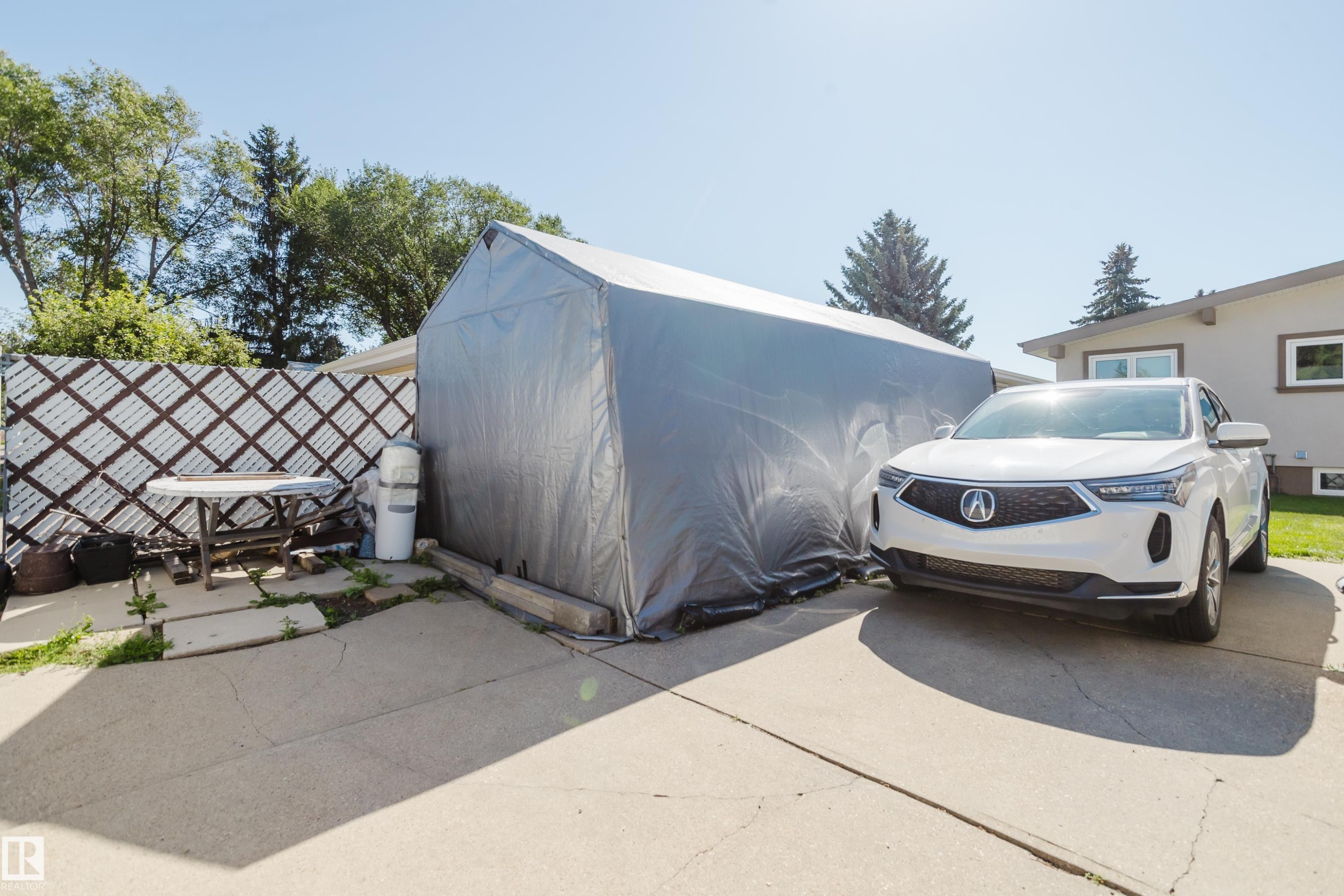 Concrete driveway and patio area, featuring a temporary storage structure and a decorative lattice fence - 10924 35A Avenue Nw, Edmonton, AB