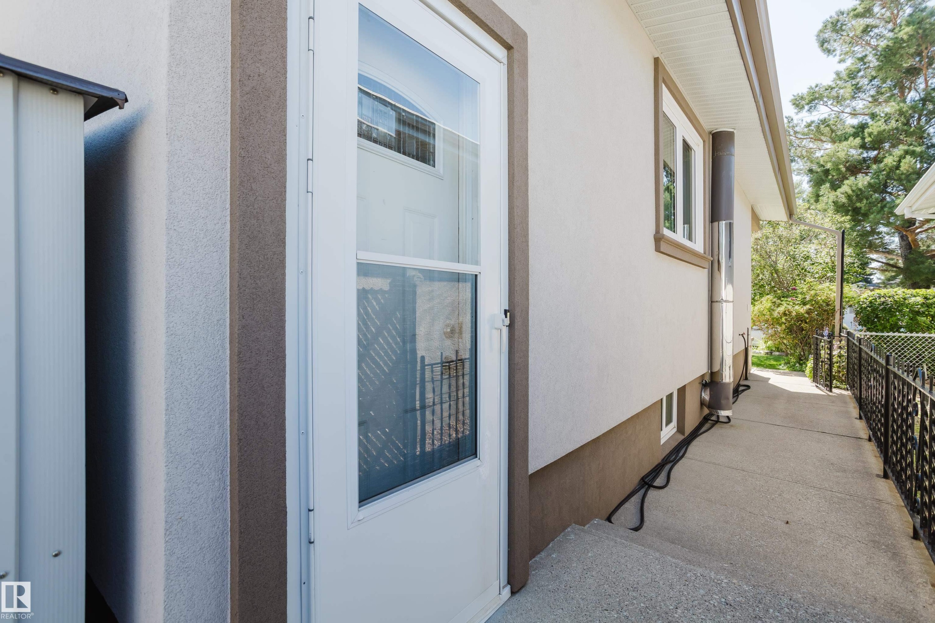 White storm door entry with glass paneling, stucco exterior, and a wrought iron style fence - 10924 35A Avenue Nw, Edmonton, AB