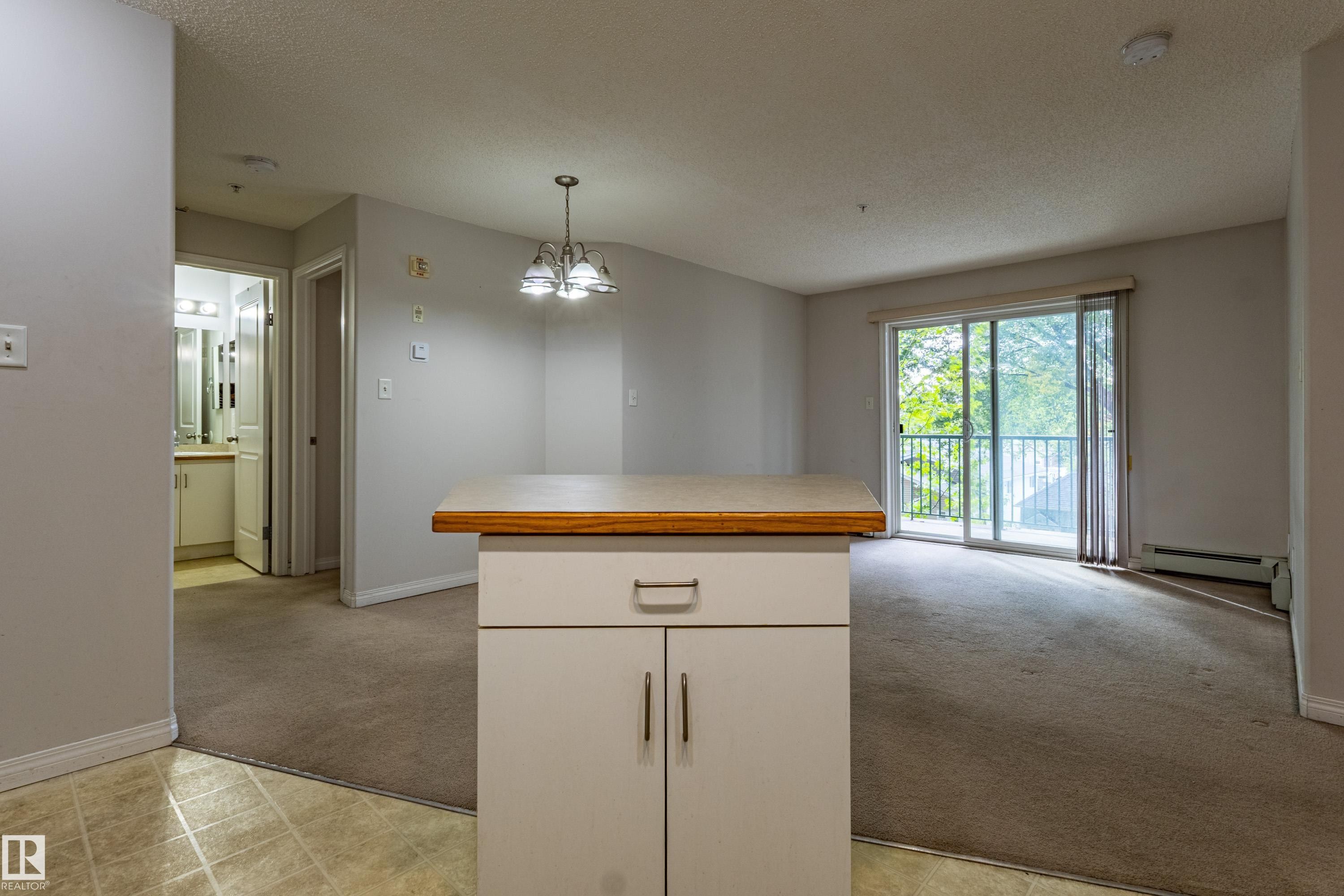 Open-concept living area with carpet flooring, a ceiling-mounted light fixture, and a sliding glass door leading to a balcony - #316 11325 83 St Nw, Edmonton, AB