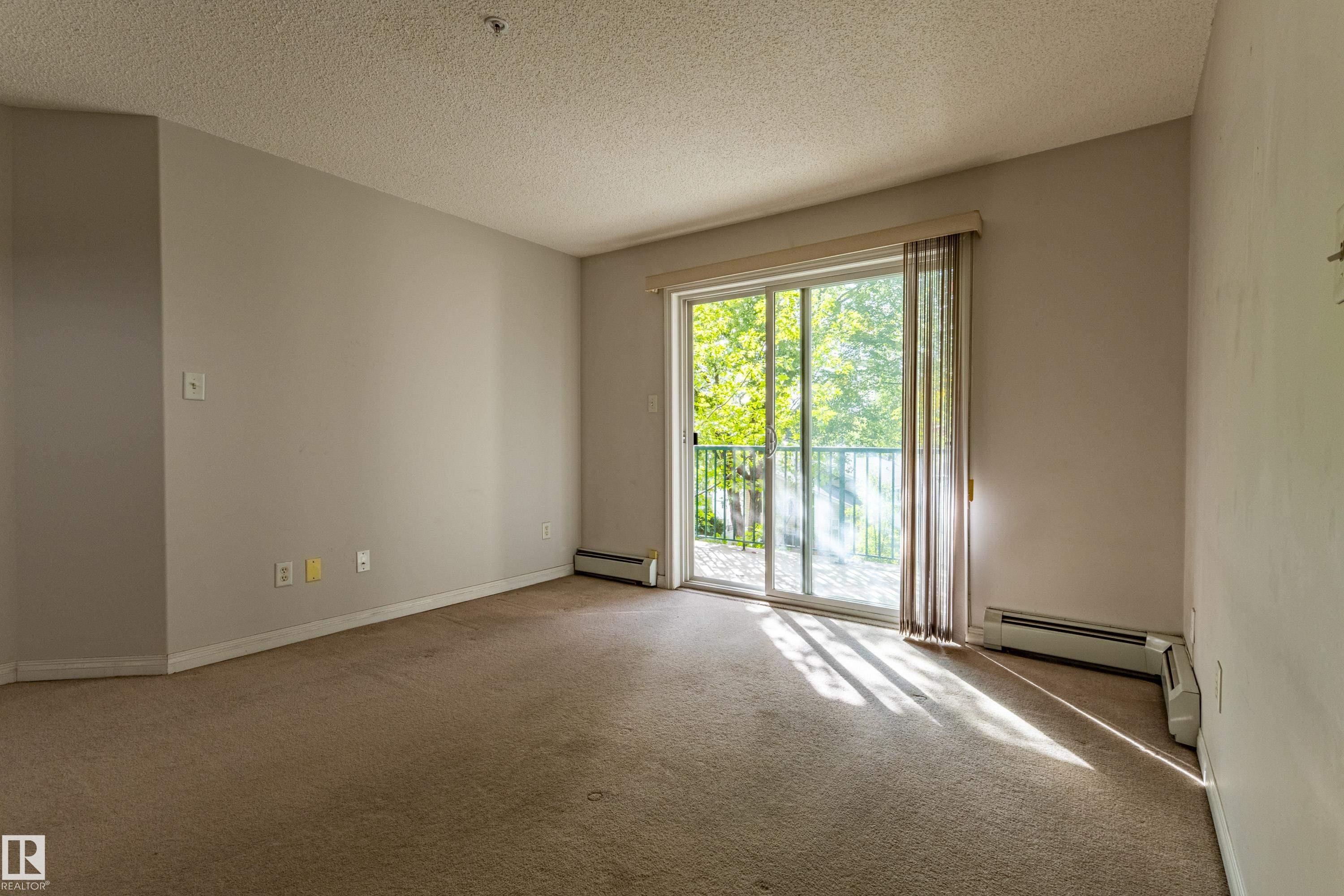 Sliding glass door leading to a balcony with metal railing, carpeted flooring, and neutral wall paint - #316 11325 83 St Nw, Edmonton, AB
