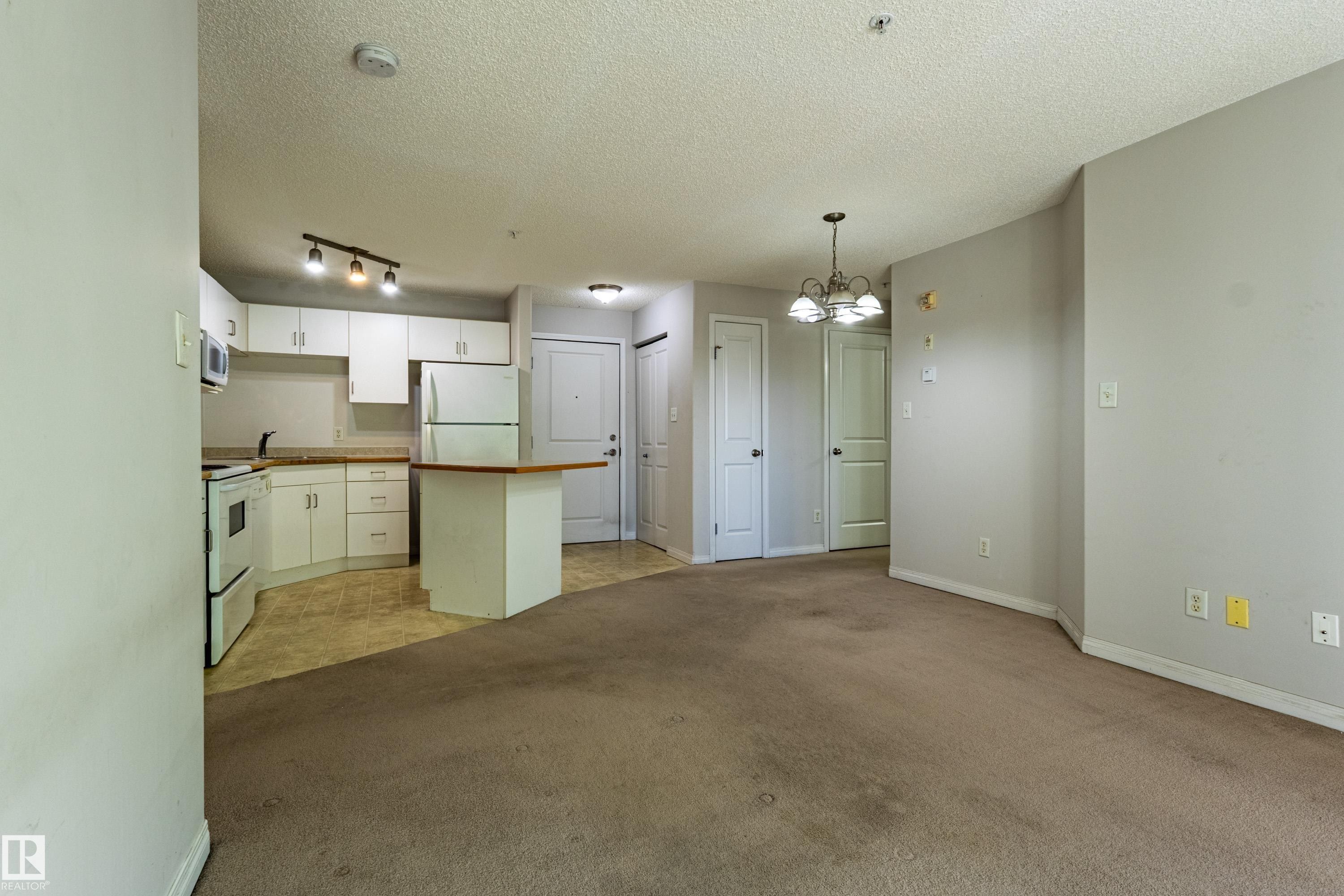 Kitchen with white cabinetry, track lighting, and a peninsula with a wood-finish countertop - #316 11325 83 St Nw, Edmonton, AB