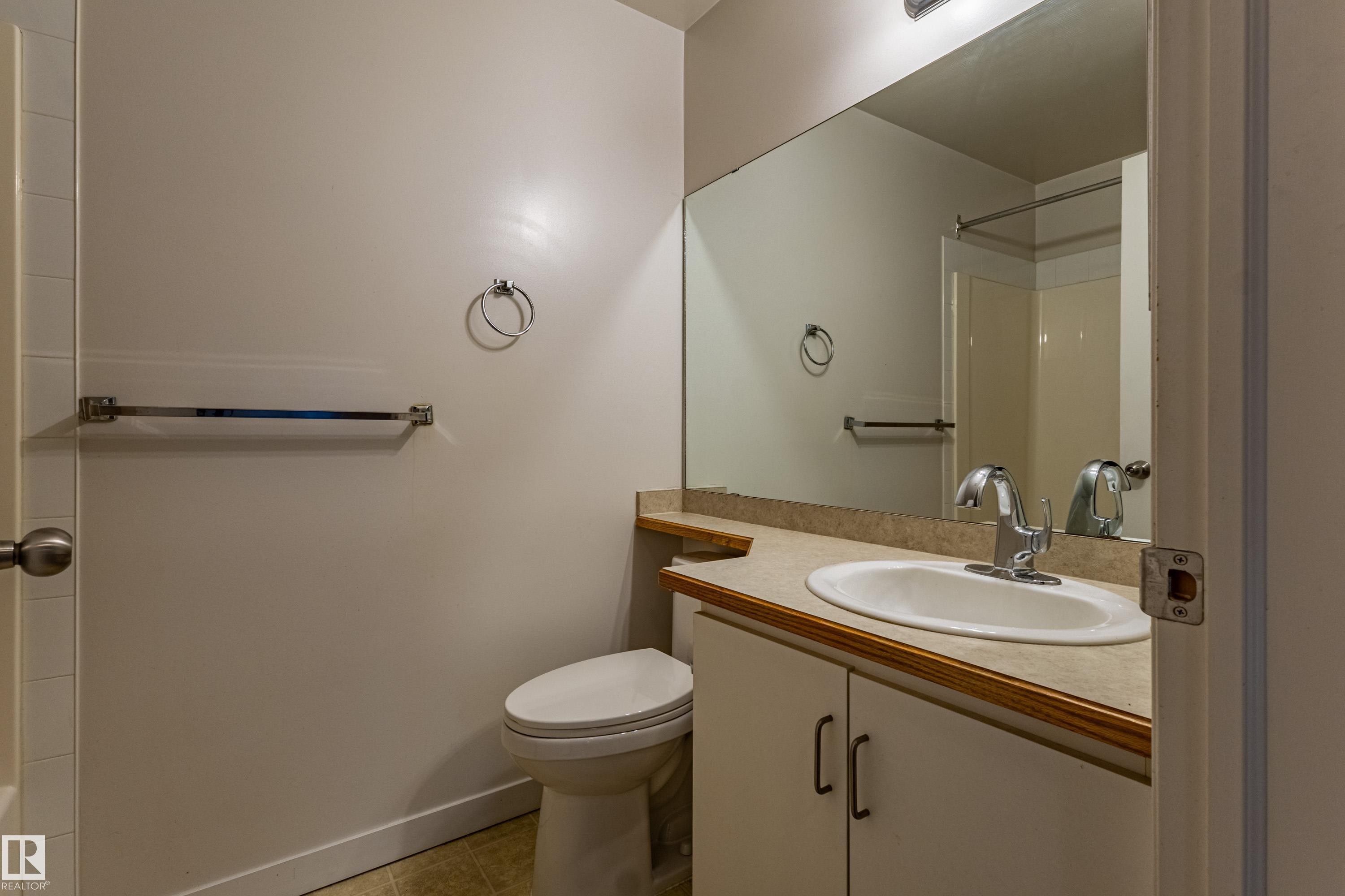 Vanity with integrated sink and chrome faucet, large wall mirror, and toilet - #316 11325 83 St Nw, Edmonton, AB