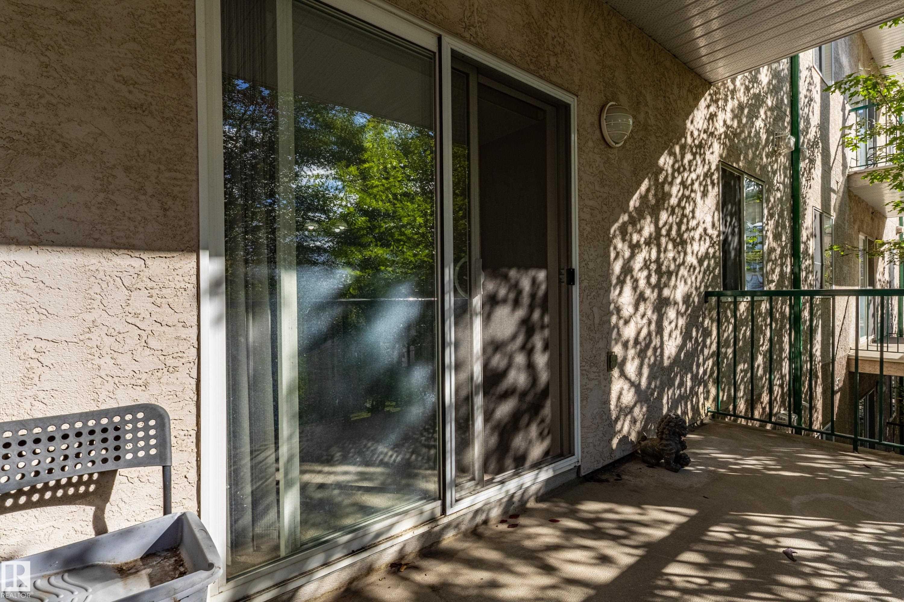 Sliding glass doors, textured stucco exterior, metal balcony railing, and exterior wall sconce - #316 11325 83 St Nw, Edmonton, AB