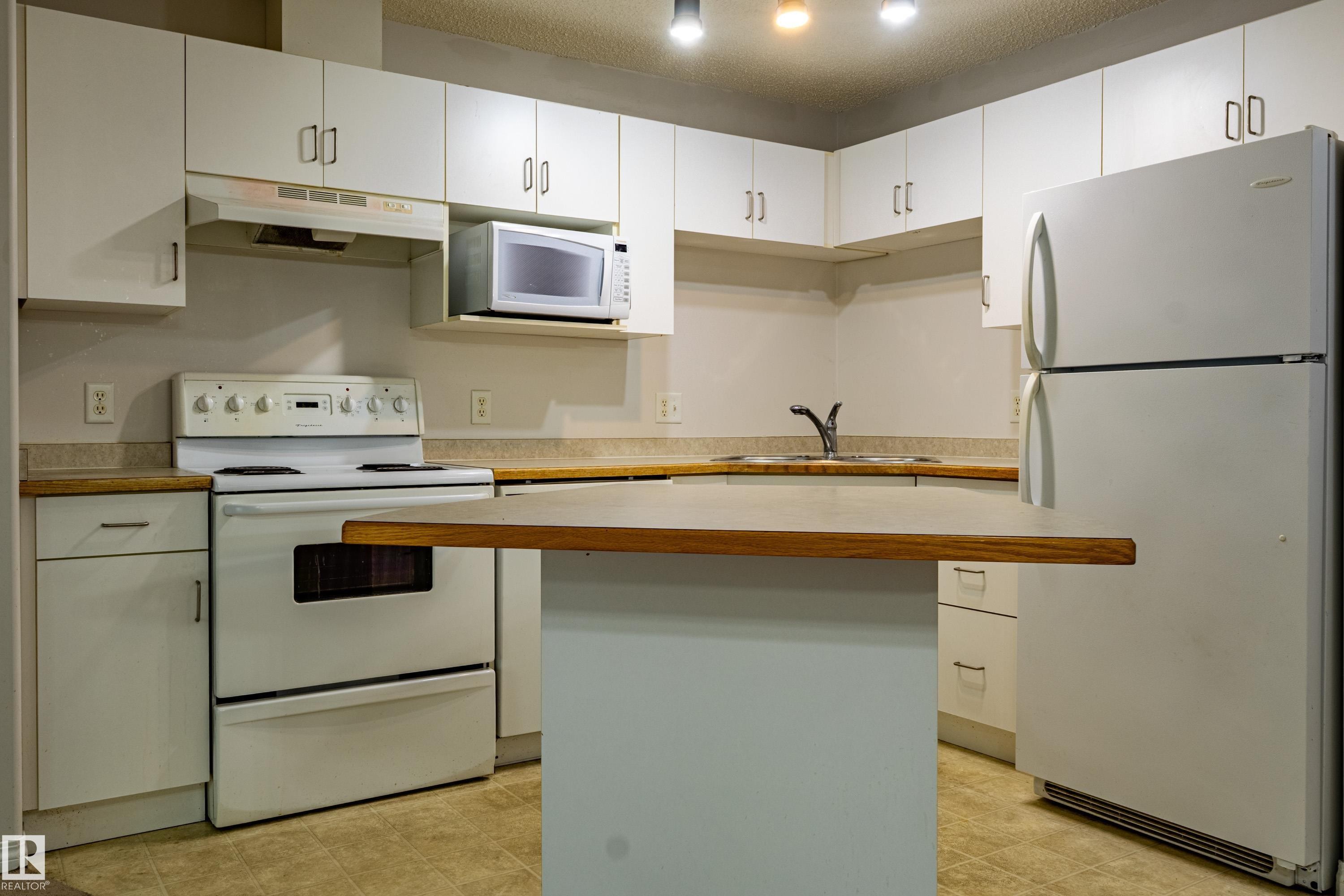Kitchen featuring white cabinetry, wood-finish countertops, and an integrated kitchen island - #316 11325 83 St Nw, Edmonton, AB