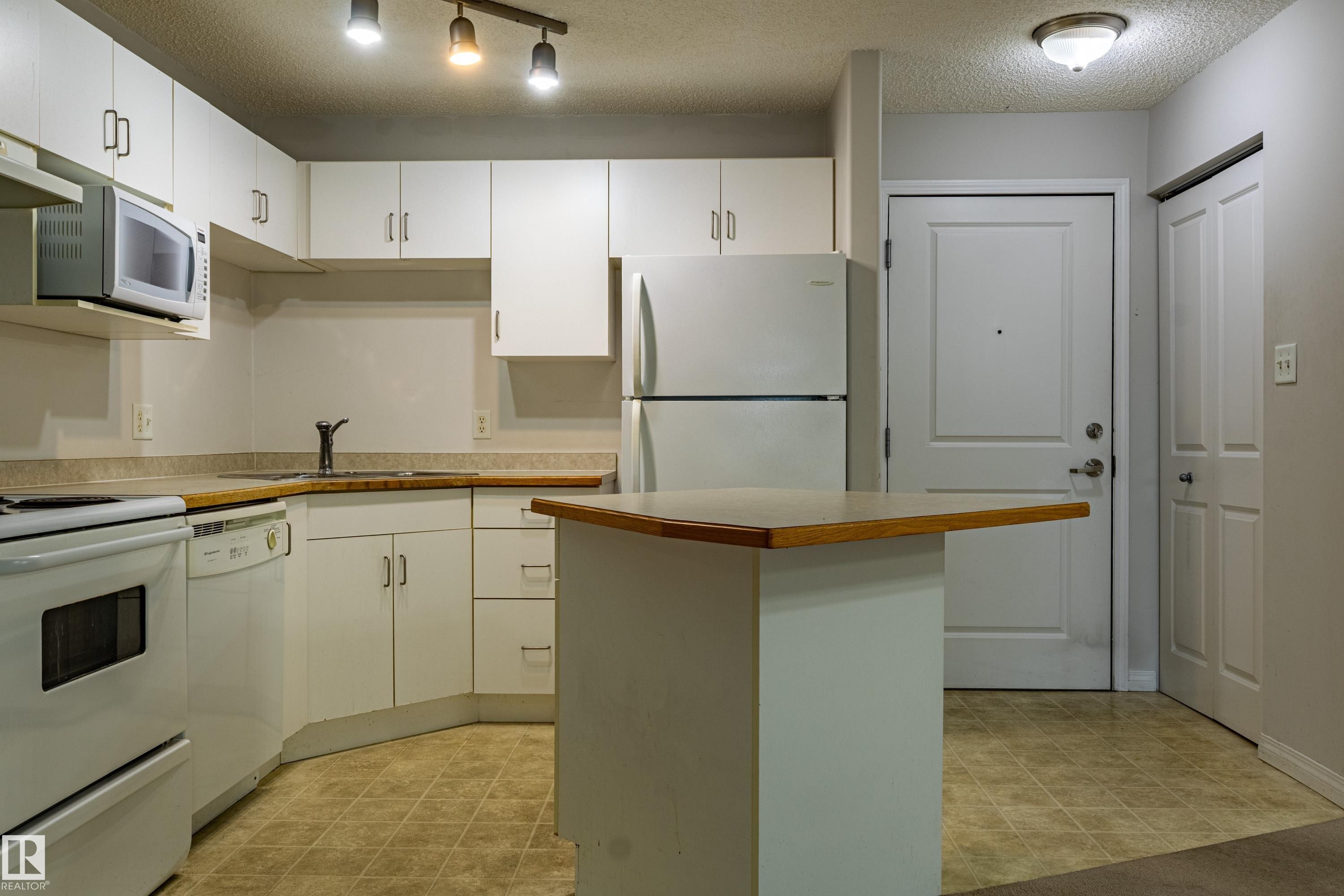 Kitchen featuring white cabinetry, built-in appliances, a corner sink, wood-finish countertops, and an integrated island - #316 11325 83 St Nw, Edmonton, AB