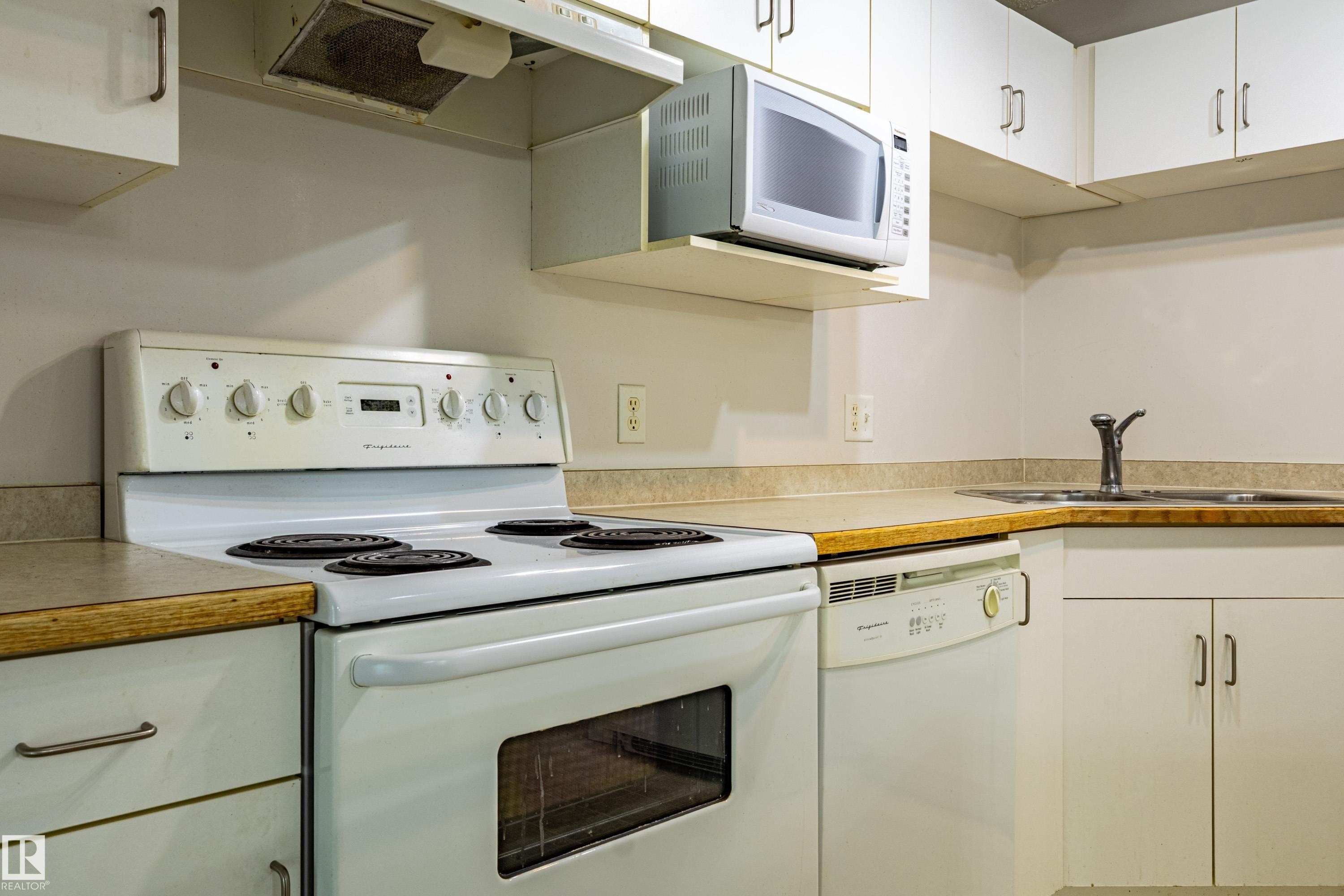 Kitchen featuring white cabinetry, an electric range, a microwave, a dishwasher, and a stainless steel sink - #316 11325 83 St Nw, Edmonton, AB