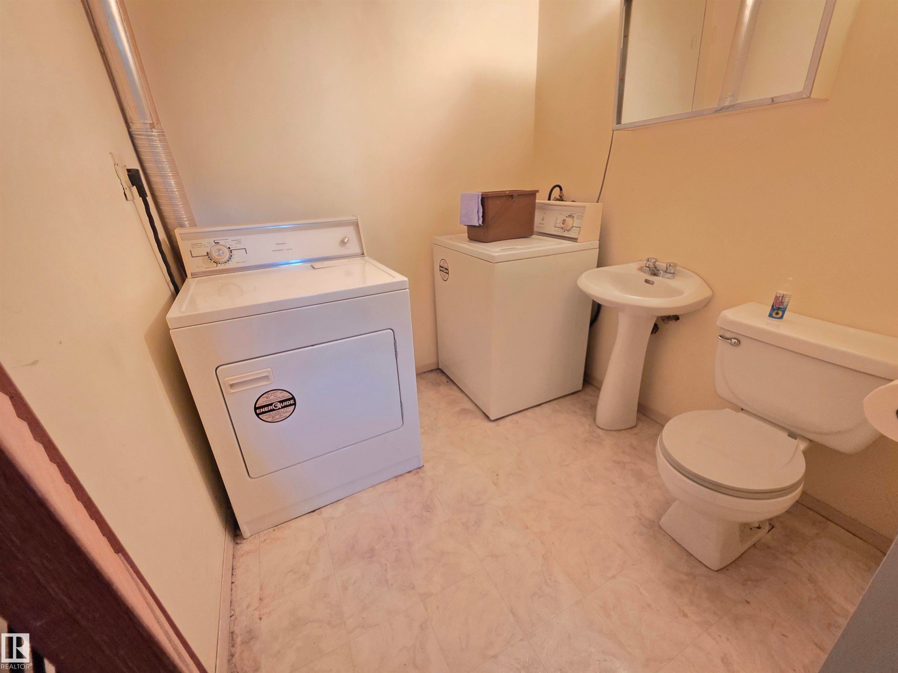 Laundry area with a freestanding washer and dryer, pedestal sink, and toilet - 10438 147 Street Nw, Edmonton, AB