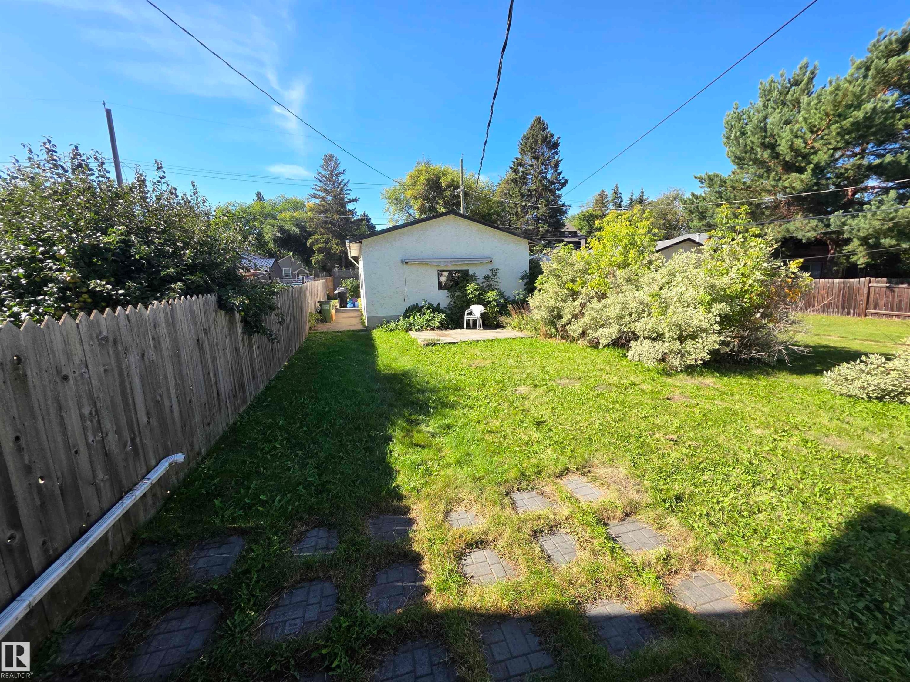 Expansive lawn area with stone pavers, bordered by a wood fence and mature trees - 10438 147 Street Nw, Edmonton, AB
