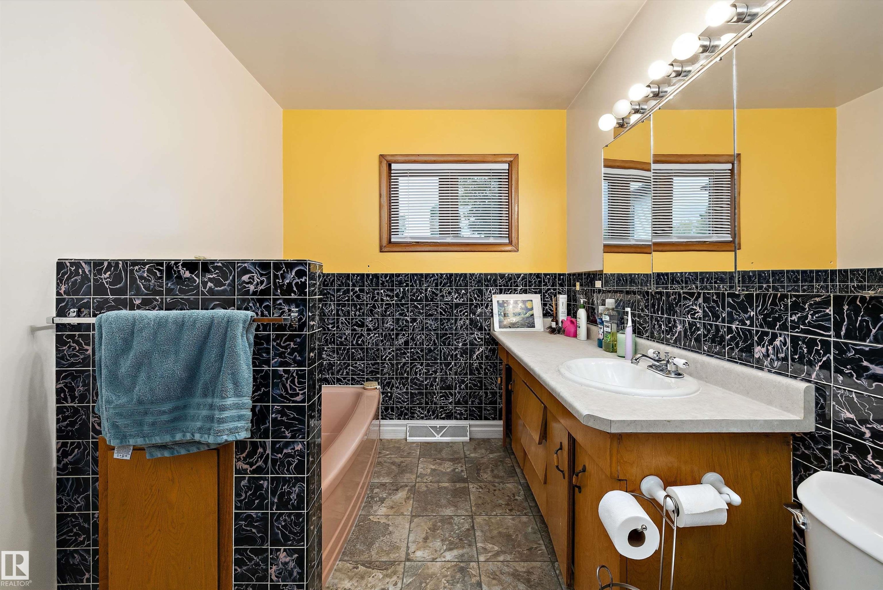 Bathroom featuring a built-in vanity with an integrated sink, a rectangular mirror with sconce lighting, and a bathtub - 10621 60A Avenue Nw, Edmonton, AB