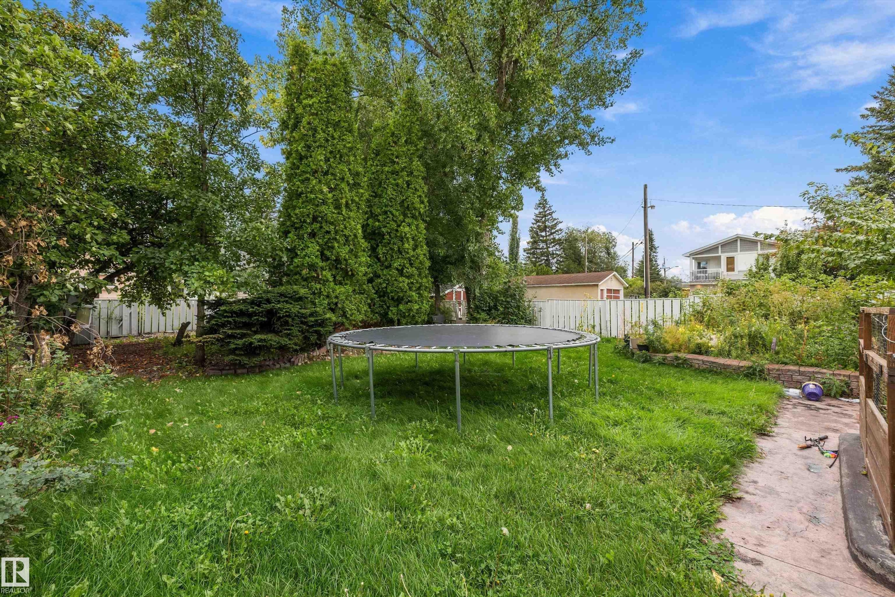 Expansive backyard featuring mature trees, established shrubs, a white picket fence, and a concrete pathway - 10621 60A Avenue Nw, Edmonton, AB