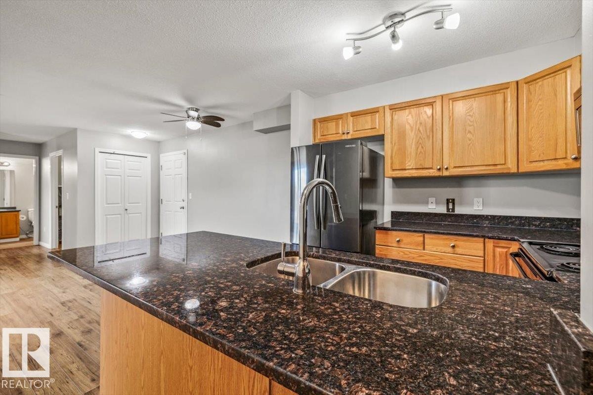 Kitchen featuring a double basin sink with a high-arc faucet, wood-finish cabinetry, and black appliances - #110 4309 33 St, Stony Plain, AB