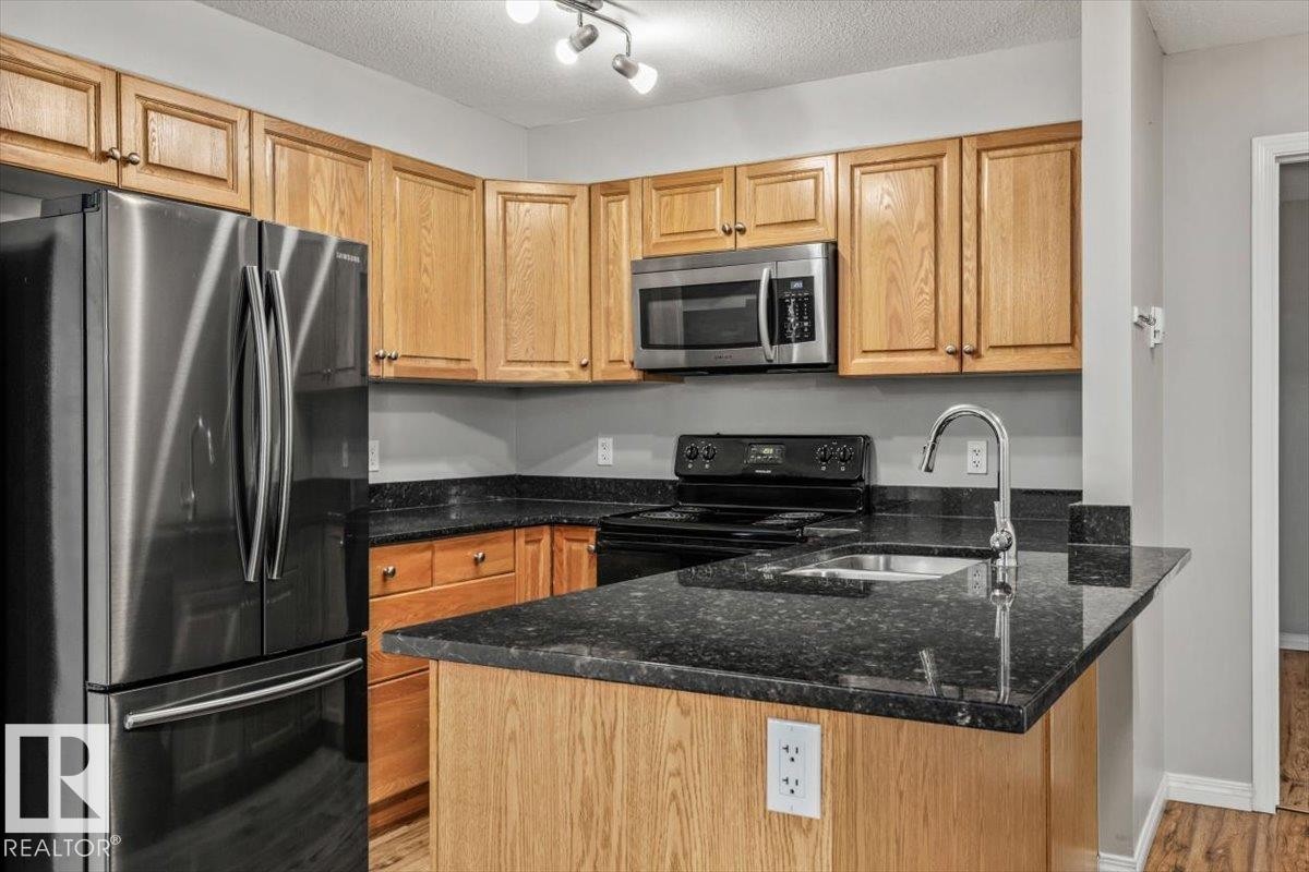 Wood-finish cabinetry paired with dark countertops, stainless steel appliances, and a built-in kitchen sink with a gooseneck faucet - #110 4309 33 St, Stony Plain, AB