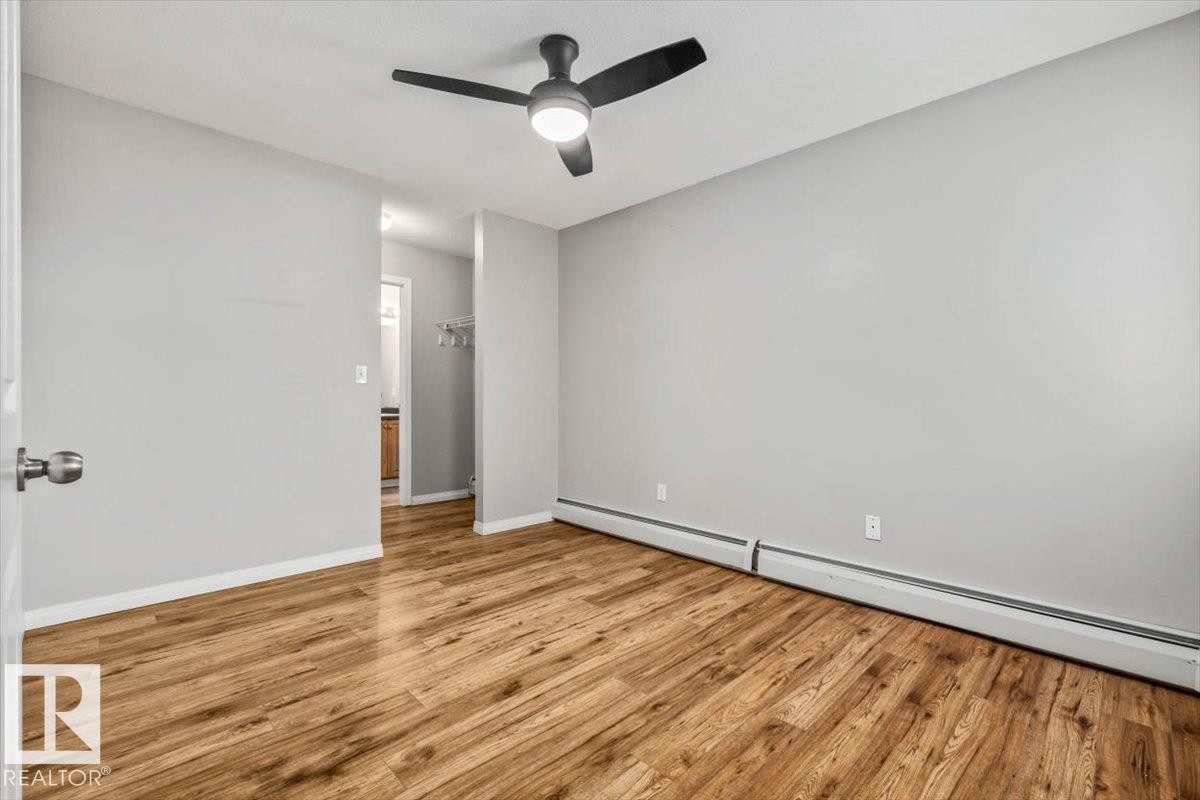 Wood-finish flooring, light gray wall paint, and a matte black ceiling fan with integrated lighting - #110 4309 33 St, Stony Plain, AB