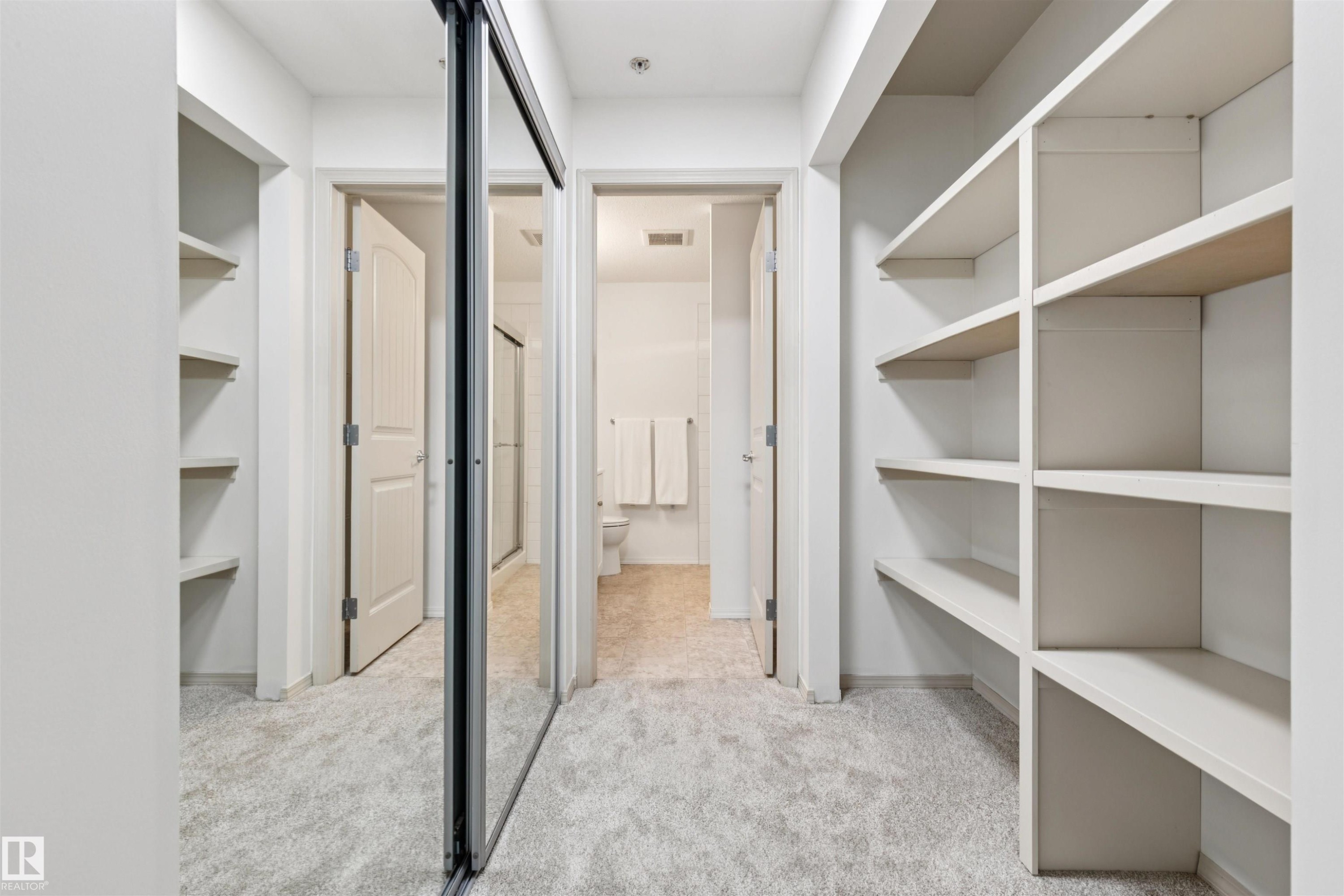Walk-in closet featuring extensive built-in shelving, mirrored sliding closet doors, and plush carpet flooring - #353 2096 Blackmud Creek Dr Sw, Edmonton, AB - Indoor With Storage