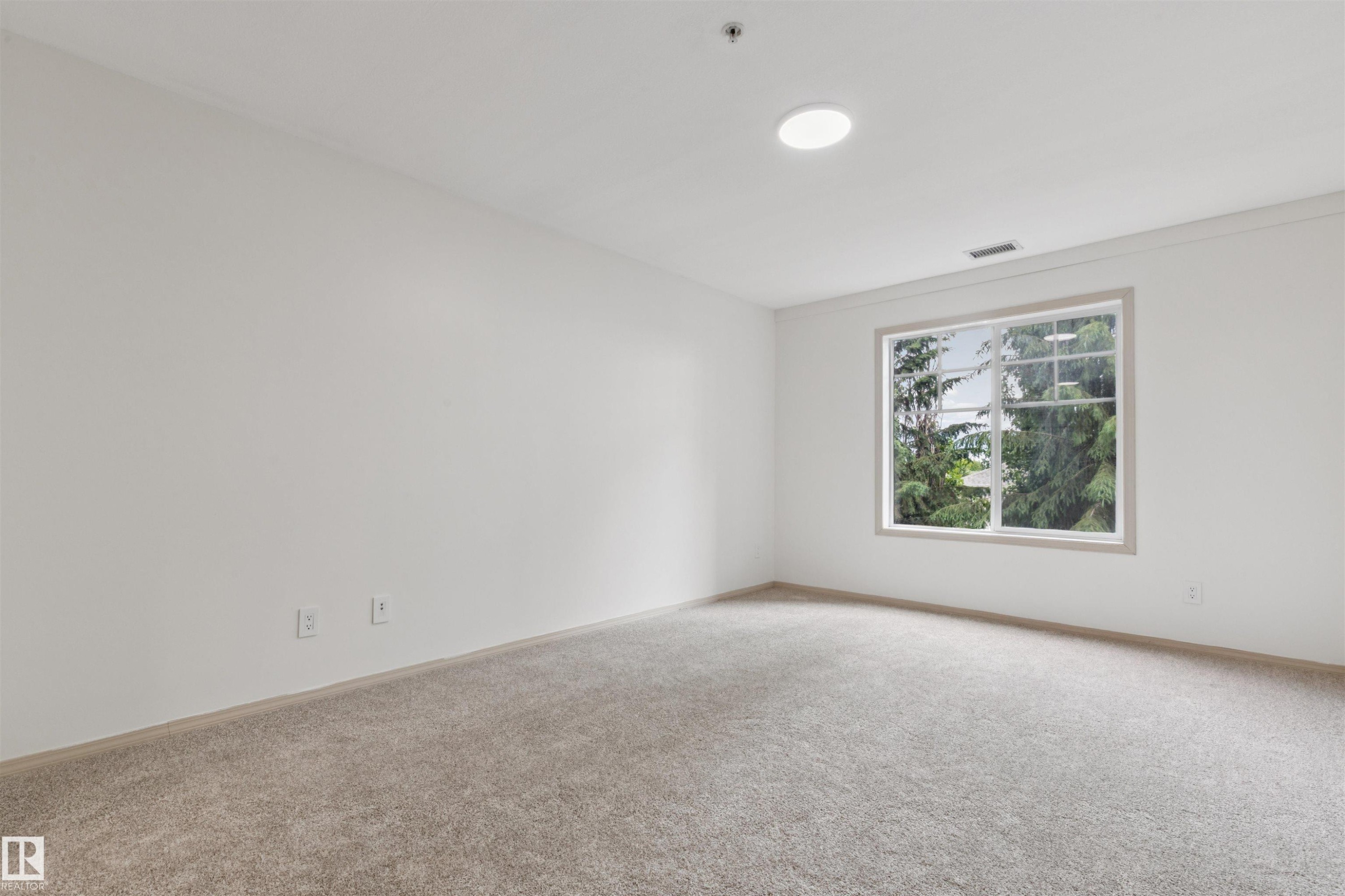 Bright room featuring a large window, plush carpeting, white walls, and a circular ceiling light fixture - #353 2096 Blackmud Creek Dr Sw, Edmonton, AB - Indoor Photo Showing Other Room