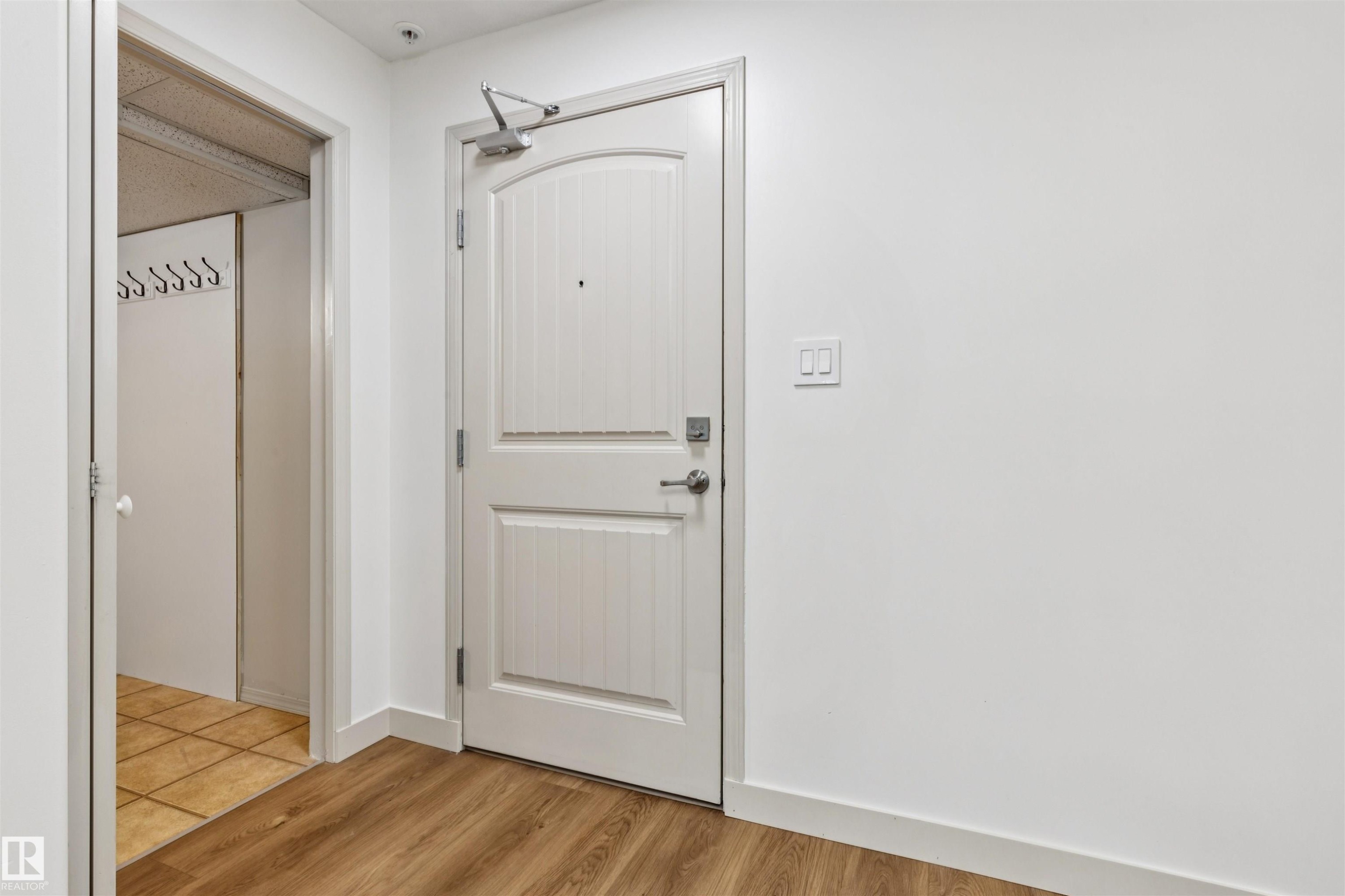 Entryway featuring a white paneled door with door closer hardware, brushed nickel hardware, and wood-finish flooring - #353 2096 Blackmud Creek Dr Sw, Edmonton, AB - Indoor Photo Showing Other Room