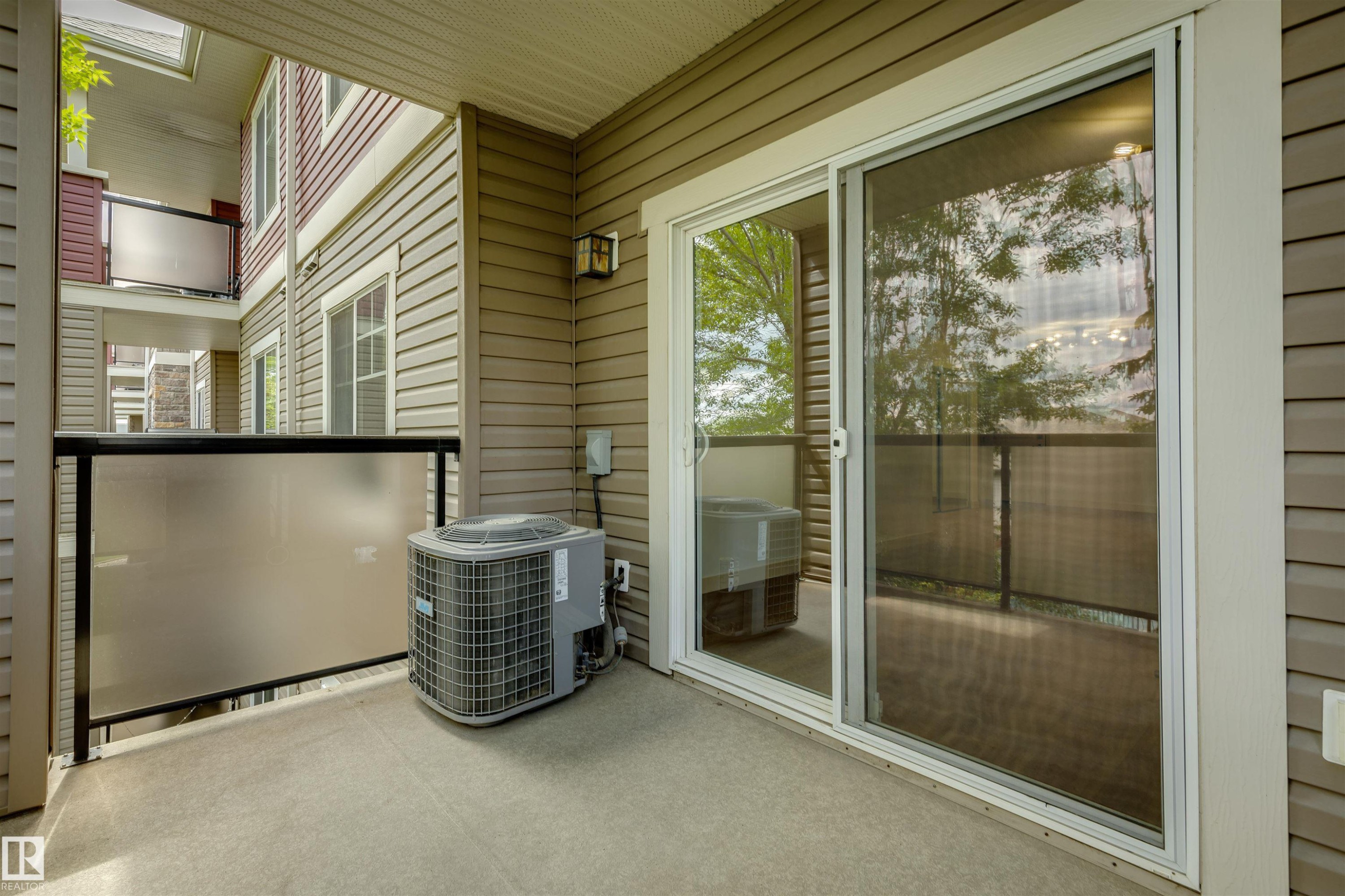 Private balcony featuring textured concrete flooring, frosted glass panel railing with a black metal frame, and a white-framed sliding glass door - #353 2096 Blackmud Creek Dr Sw, Edmonton, AB - Outdoor With Balcony With Exterior
