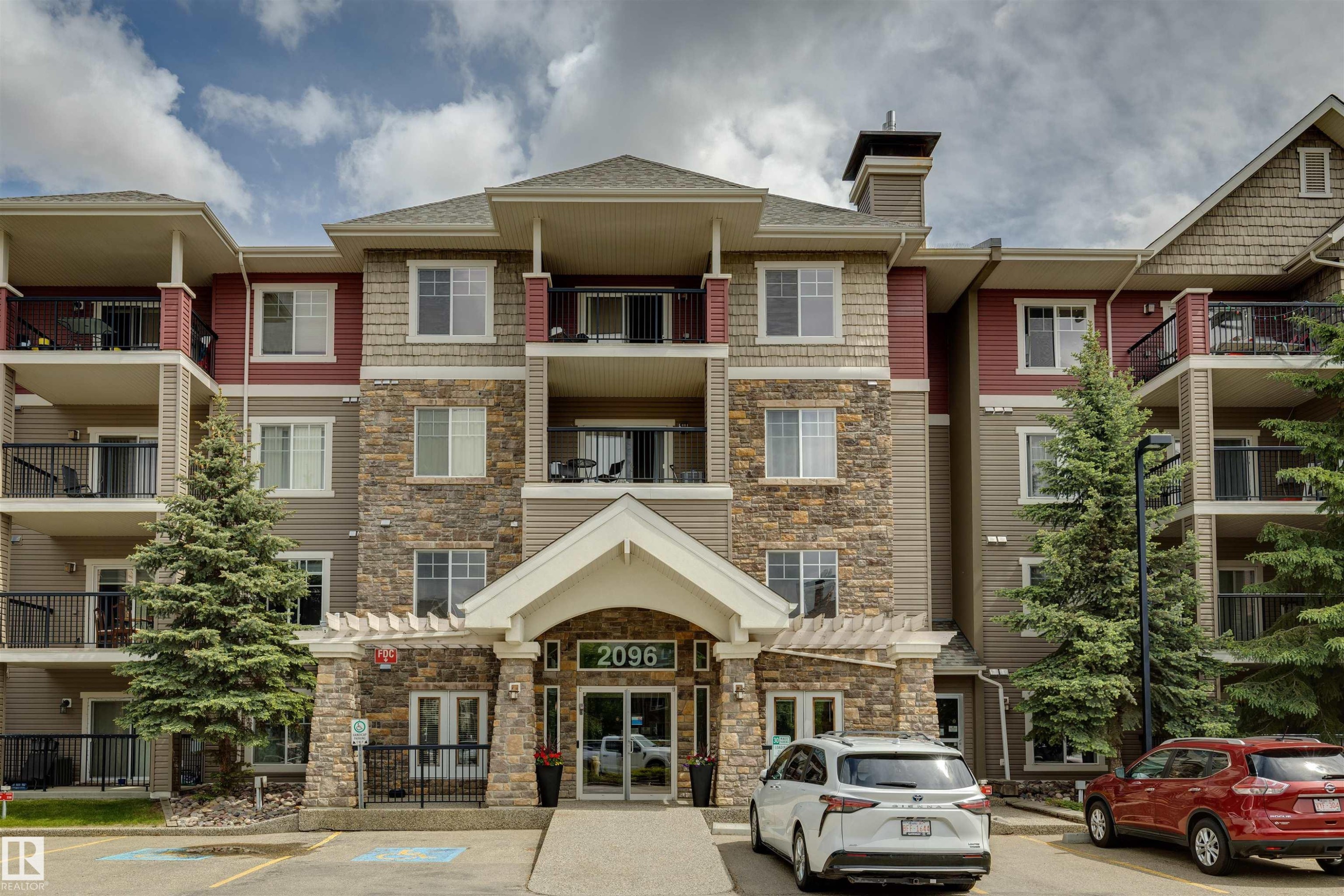 Contemporary multi-story building featuring stone veneer accents, multiple private balconies, and a covered entry - #353 2096 Blackmud Creek Dr Sw, Edmonton, AB - Outdoor With Balcony With Facade
