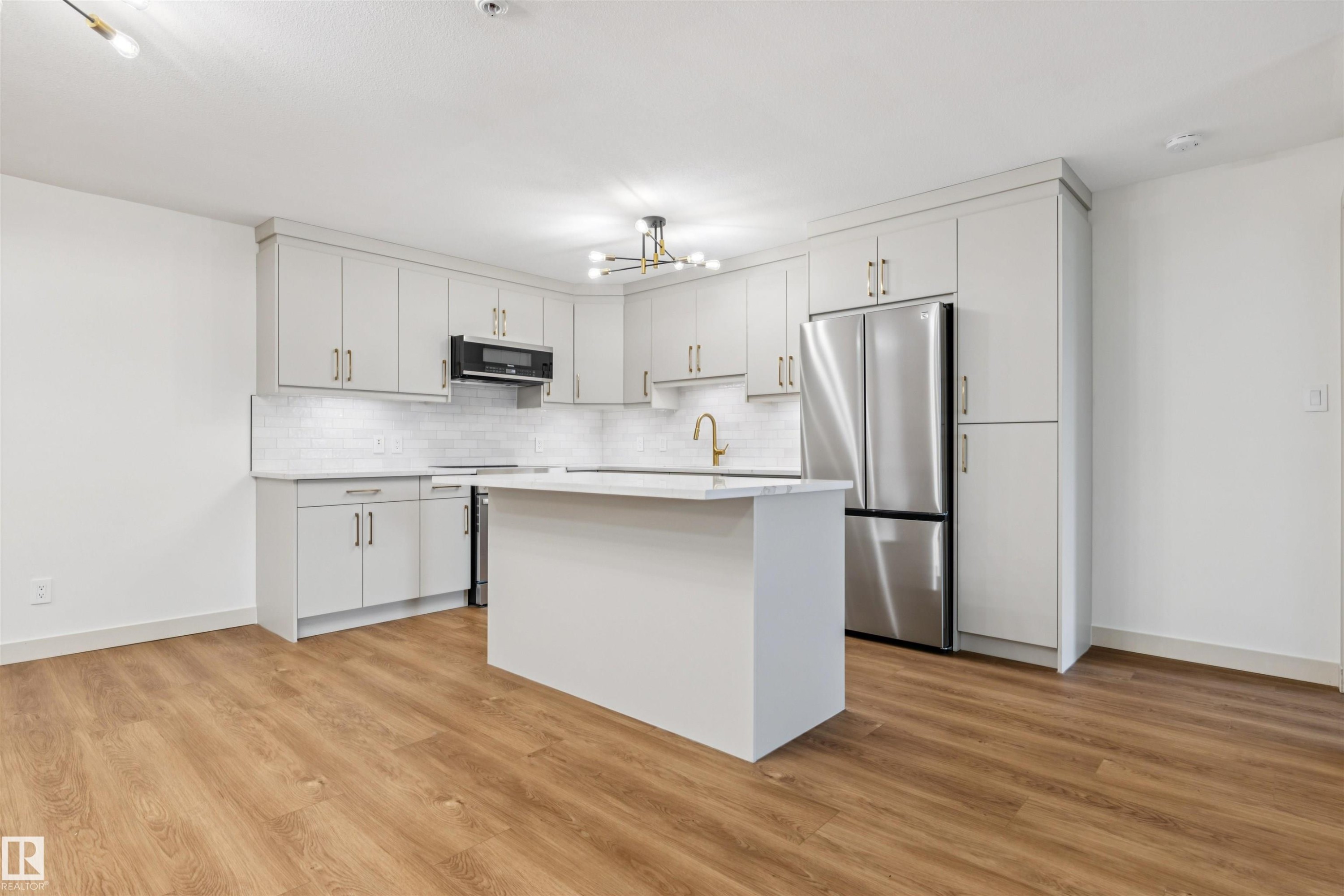 Modern kitchen featuring light cabinetry, stainless steel appliances, a center island, subway tile backsplash, and wood-finish flooring - #353 2096 Blackmud Creek Dr Sw, Edmonton, AB - Indoor Photo Showing Kitchen With Stainless Steel Kitchen With Upgraded Kitchen
