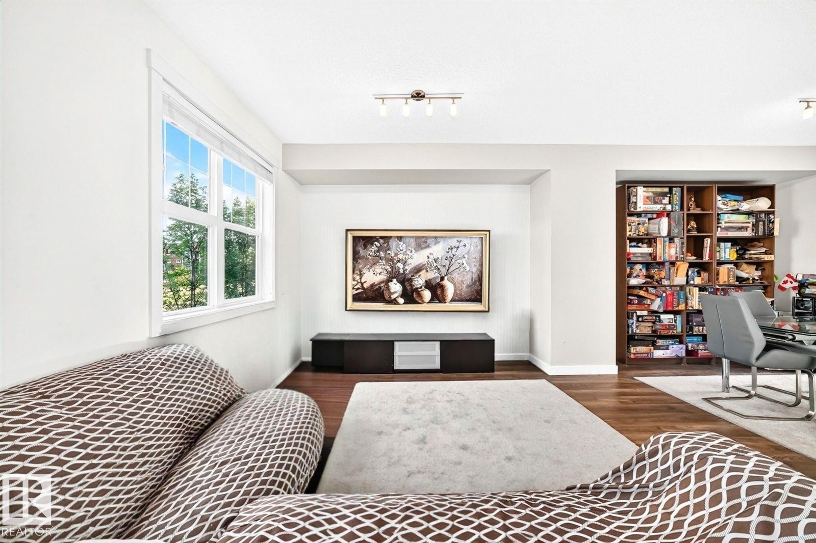 Recessed wall for media, wood-finish flooring, built-in shelving, white trim window, and overhead track lighting - #20 8315 180 Av Nw, Edmonton, AB