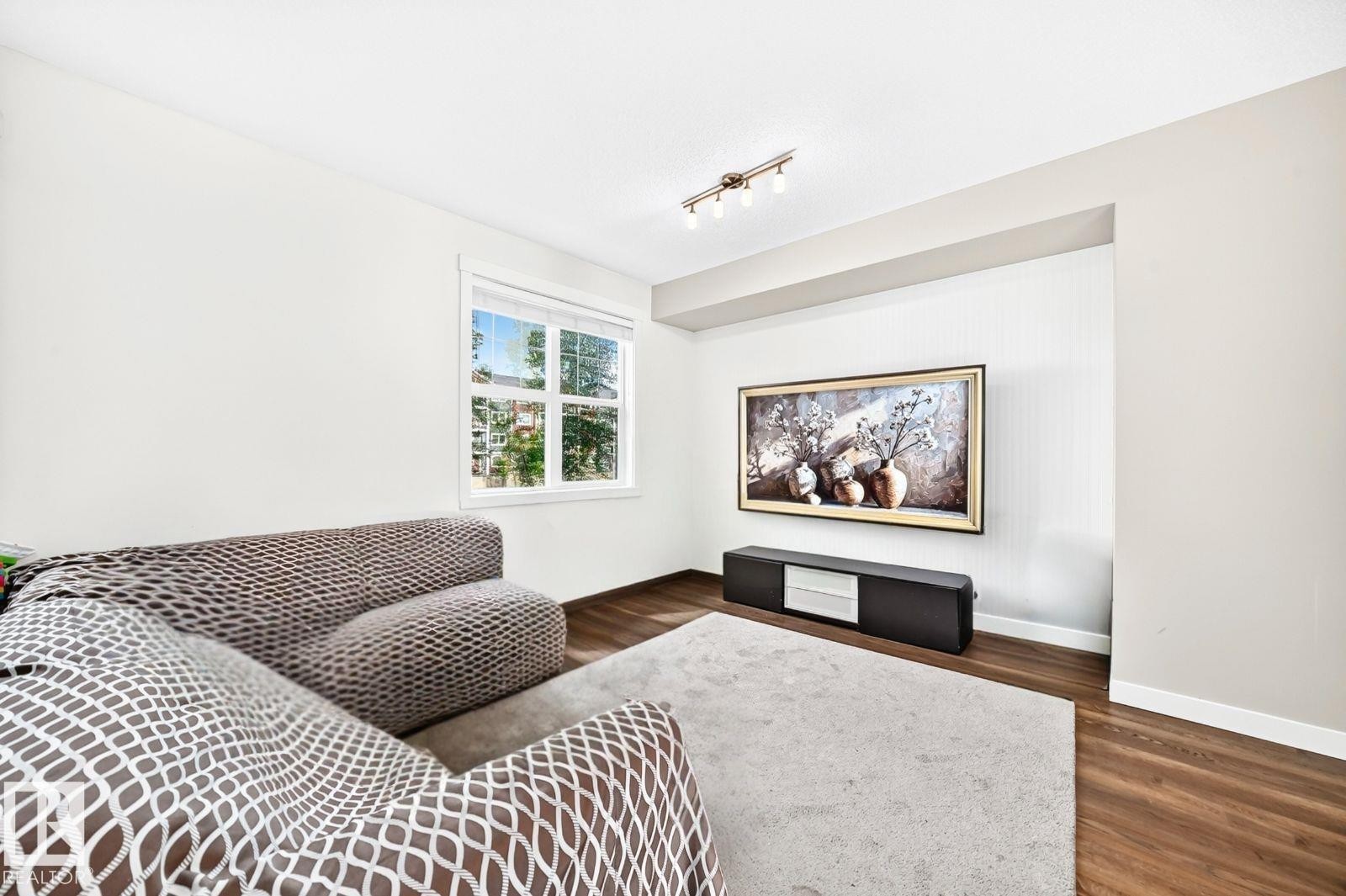 Recessed media wall, track lighting, wood-finish flooring, white trim, and a white framed window - #20 8315 180 Av Nw, Edmonton, AB