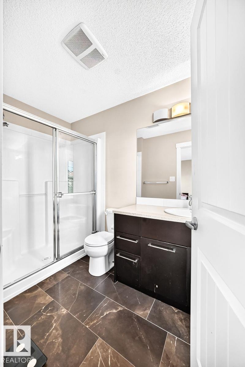 Spacious bathroom with a walk-in shower, dark wood-finish vanity, and light-toned countertop - #20 8315 180 Av Nw, Edmonton, AB