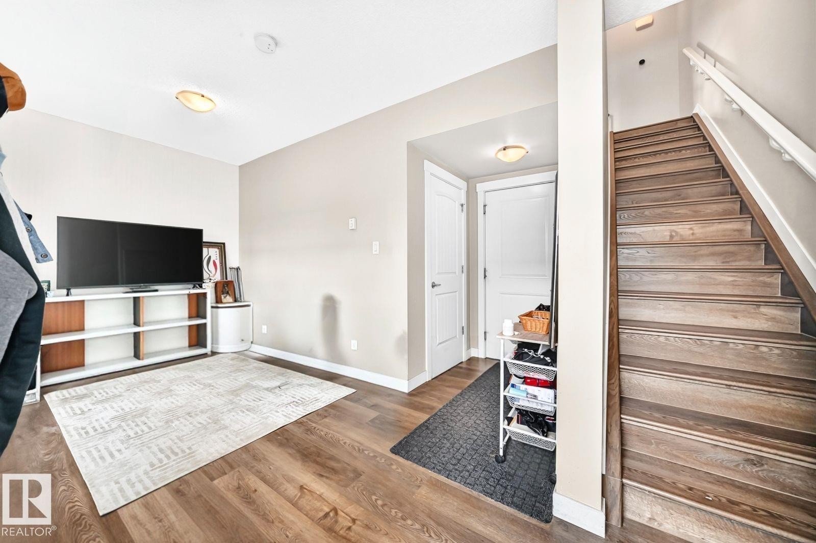 Wood-finish flooring throughout, white interior doors, staircase with wood-finish treads and white railing, and flush-mount ceiling lights - #20 8315 180 Av Nw, Edmonton, AB