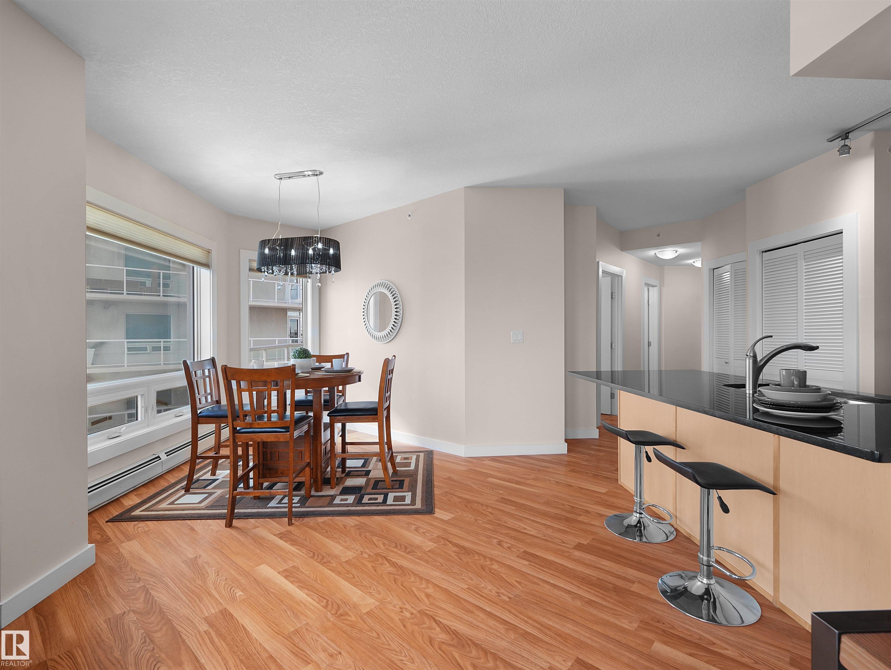 Spacious open-concept living area with wood-finish flooring, a kitchen island with seating, and a dining area with a chandelier - #1601 10136 104 St Nw, Edmonton, AB