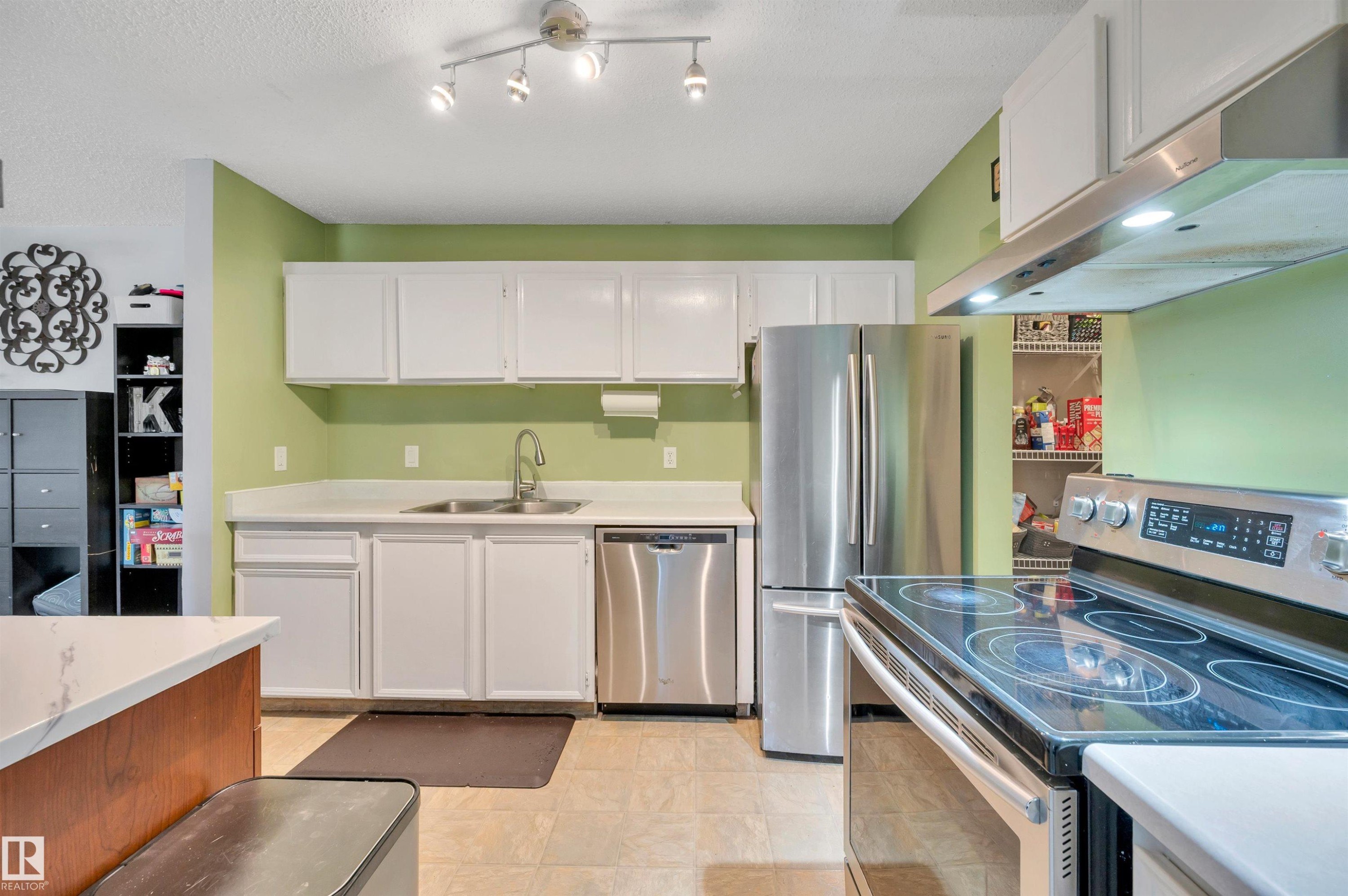 Kitchen featuring white cabinetry, stainless steel appliances, a dual basin sink, and track lighting - 15017 26 Street Nw, Edmonton, AB