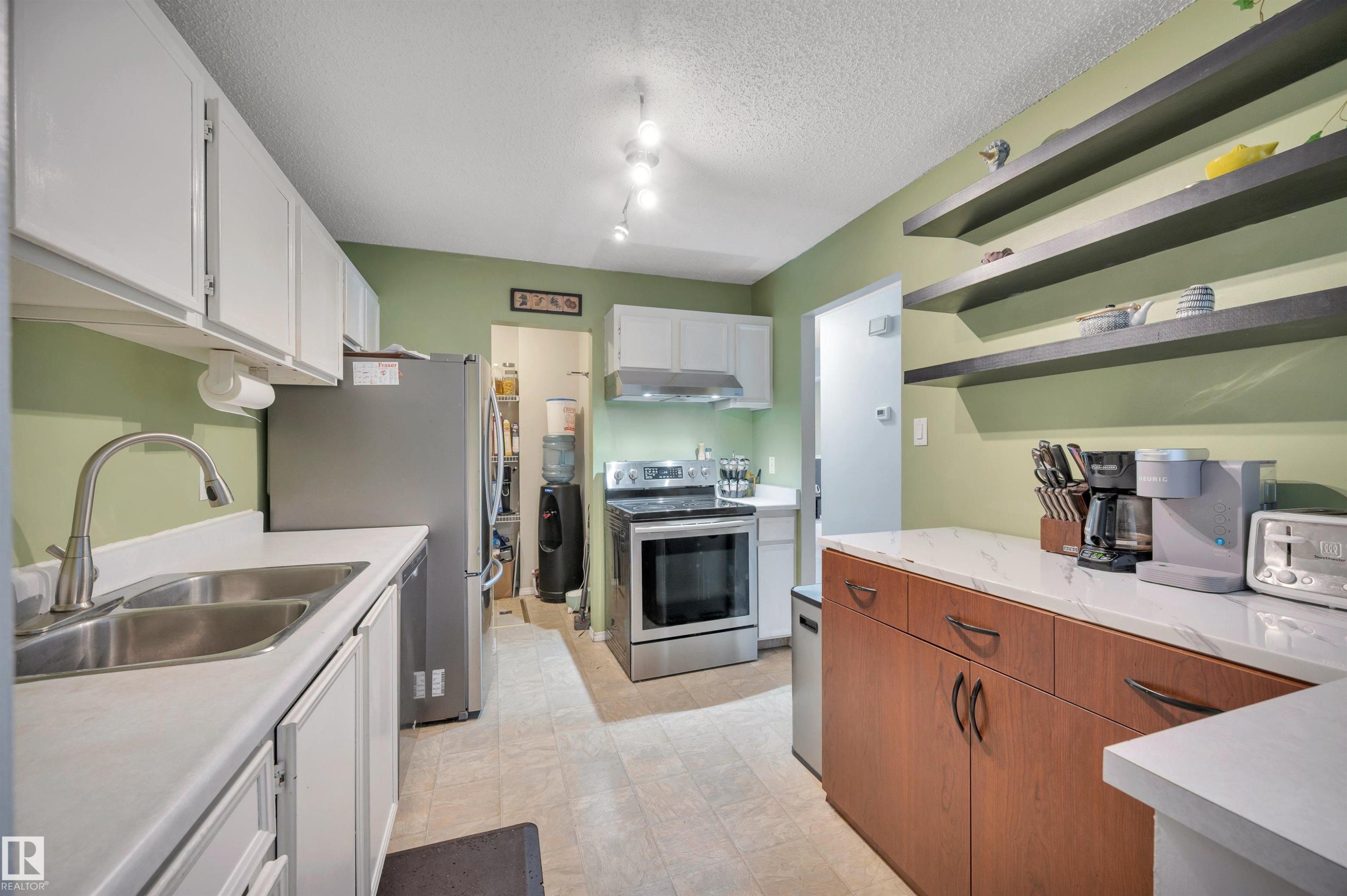 Kitchen featuring white cabinetry, stainless steel appliances, open shelving, and wood-finish lower cabinetry - 15017 26 Street Nw, Edmonton, AB