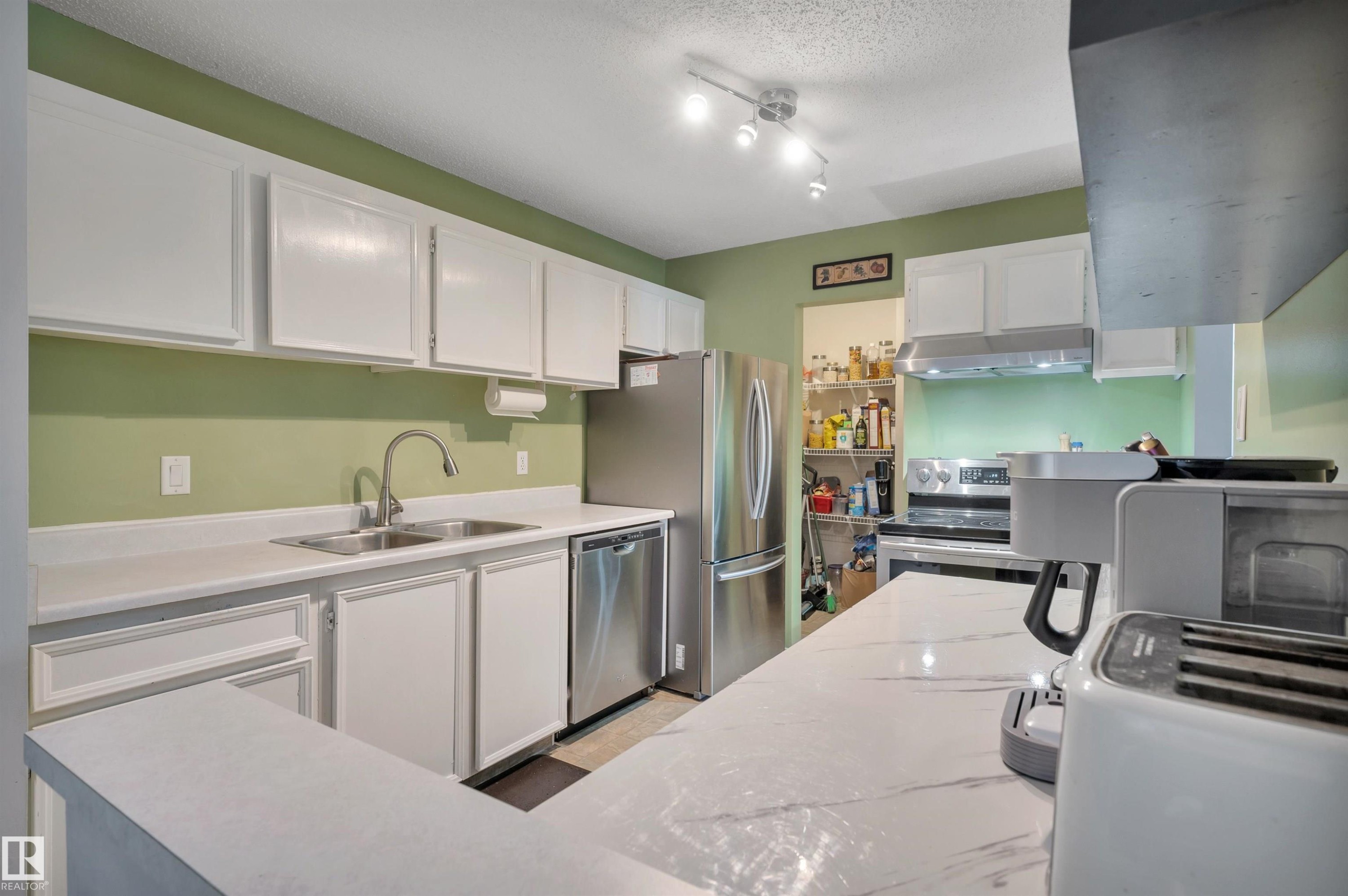 White cabinetry, stainless steel appliances, solid surface countertops, track lighting, and a double basin sink - 15017 26 Street Nw, Edmonton, AB