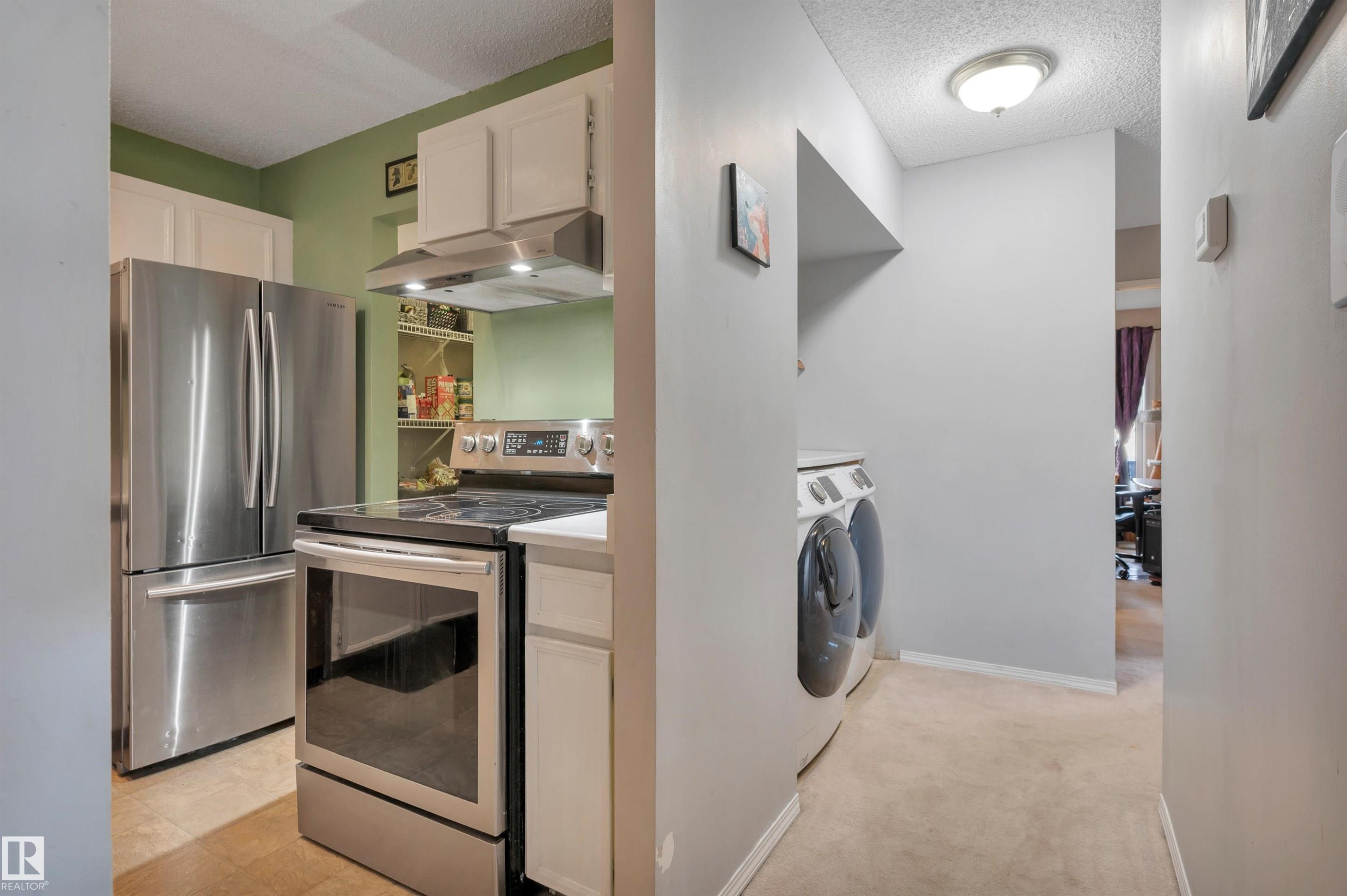 Stainless steel appliance suite, white cabinetry, light-toned flooring, and integrated laundry appliances - 15017 26 Street Nw, Edmonton, AB
