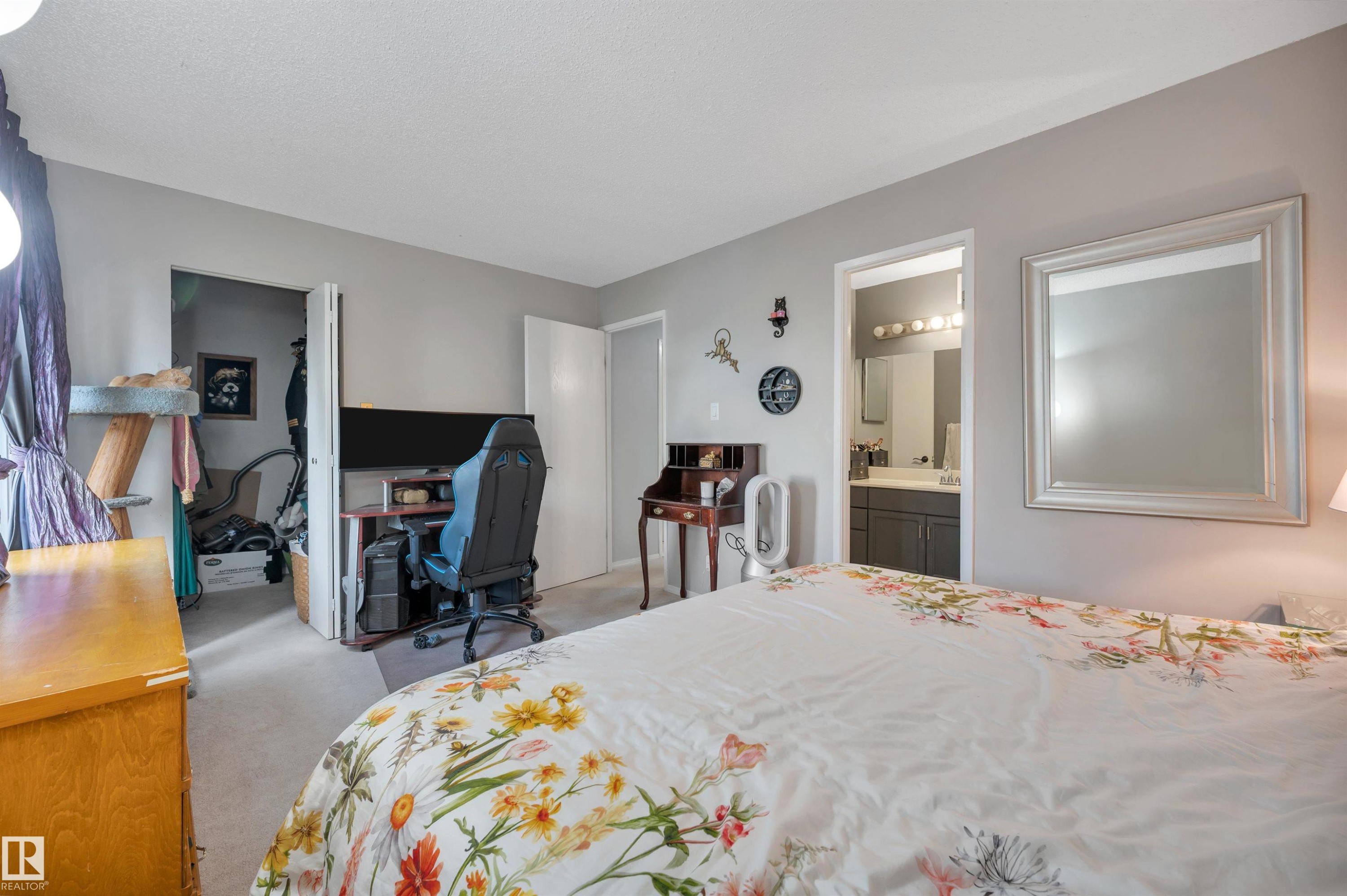 Hardwood-style dresser, light gray wall paint, doorway to bathroom featuring a vanity with a dark cabinet, and light-colored carpeting - 15017 26 Street Nw, Edmonton, AB