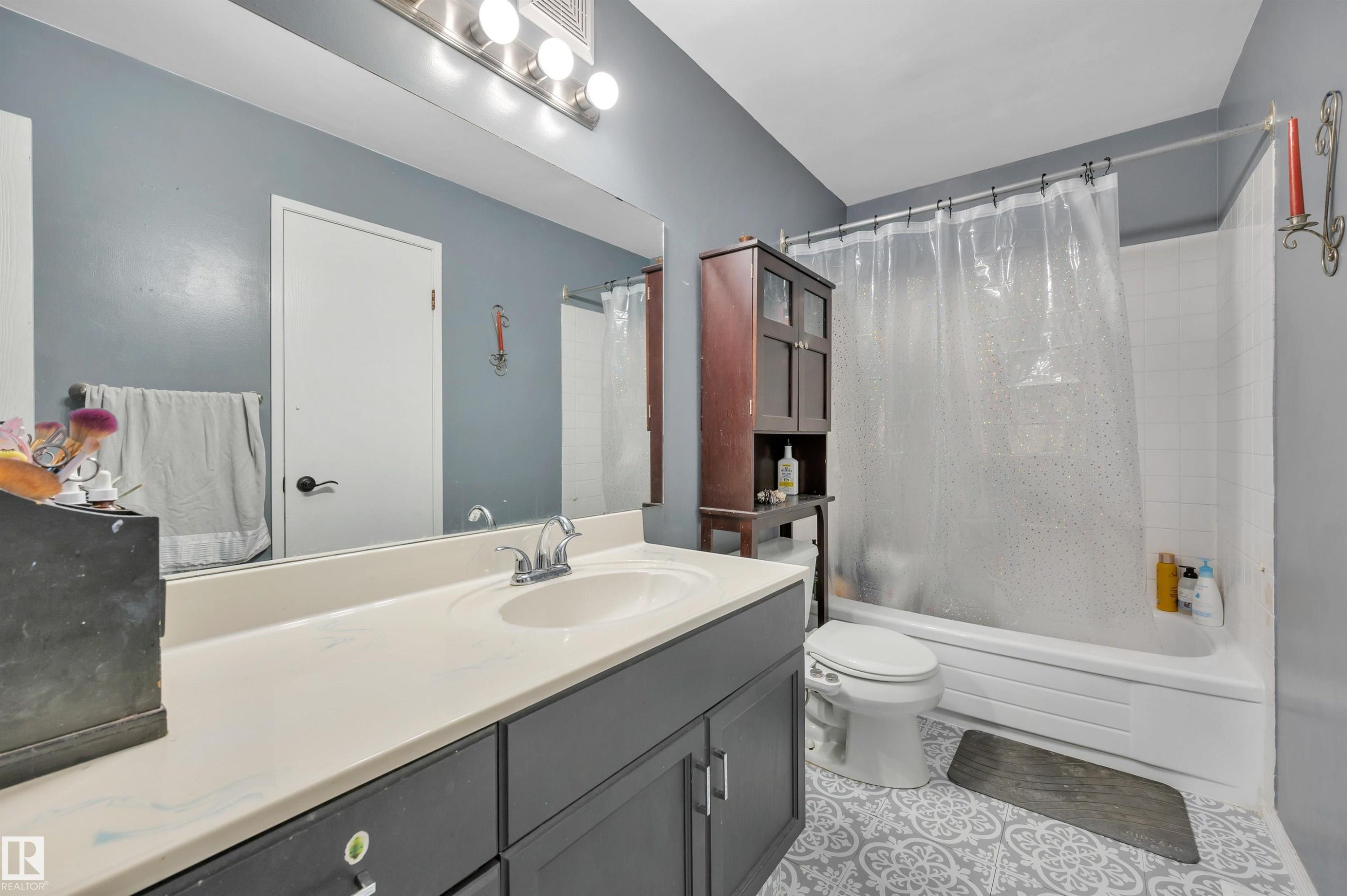 Vanity with an integrated sink and base cabinetry, patterned floor tile, white subway tile bath surround, and overhead vanity lighting - 15017 26 Street Nw, Edmonton, AB