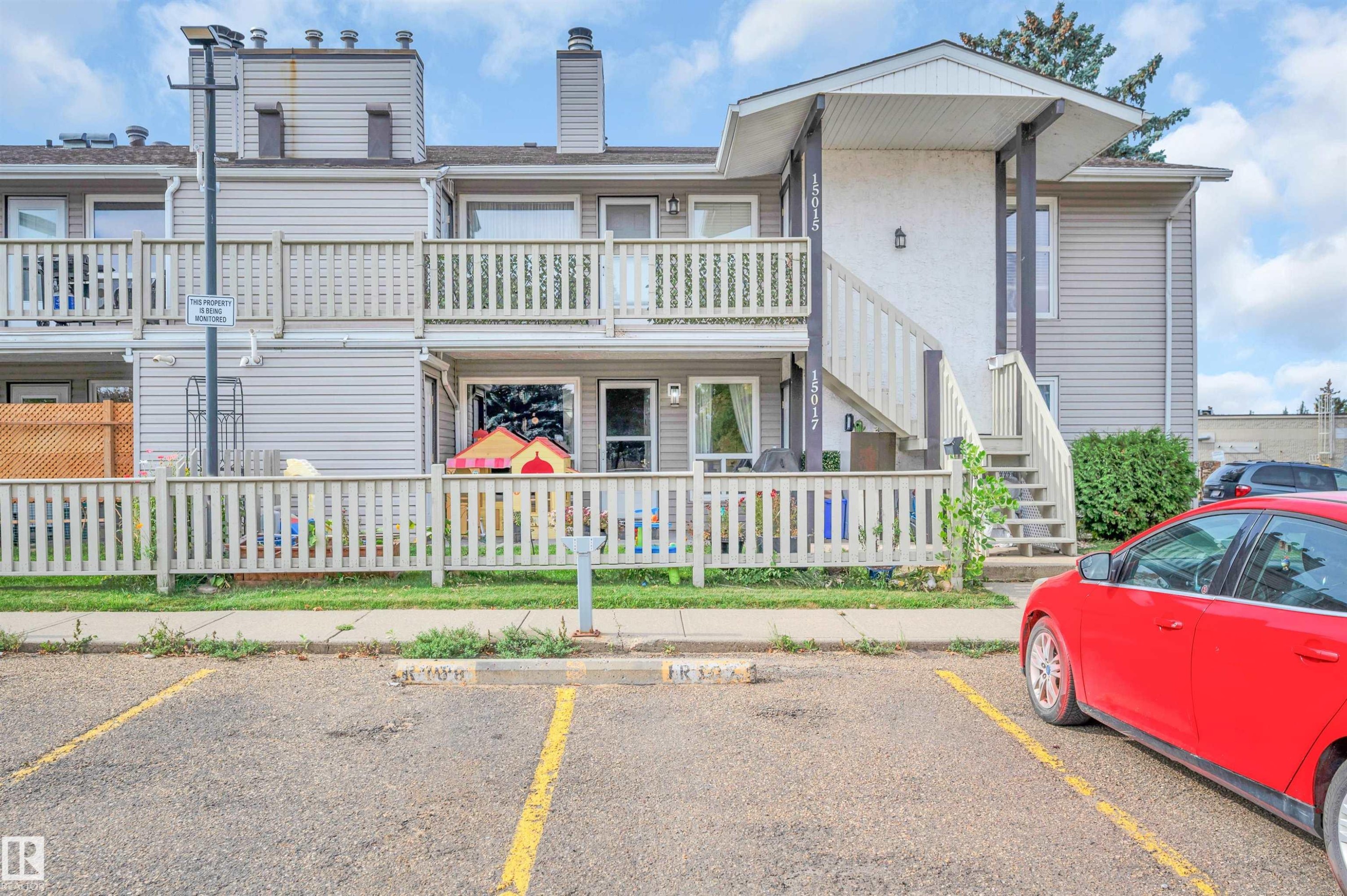 Exterior featuring multiple balconies with wooden railings, siding facade, a front entry staircase, and designated paved parking - 15017 26 Street Nw, Edmonton, AB