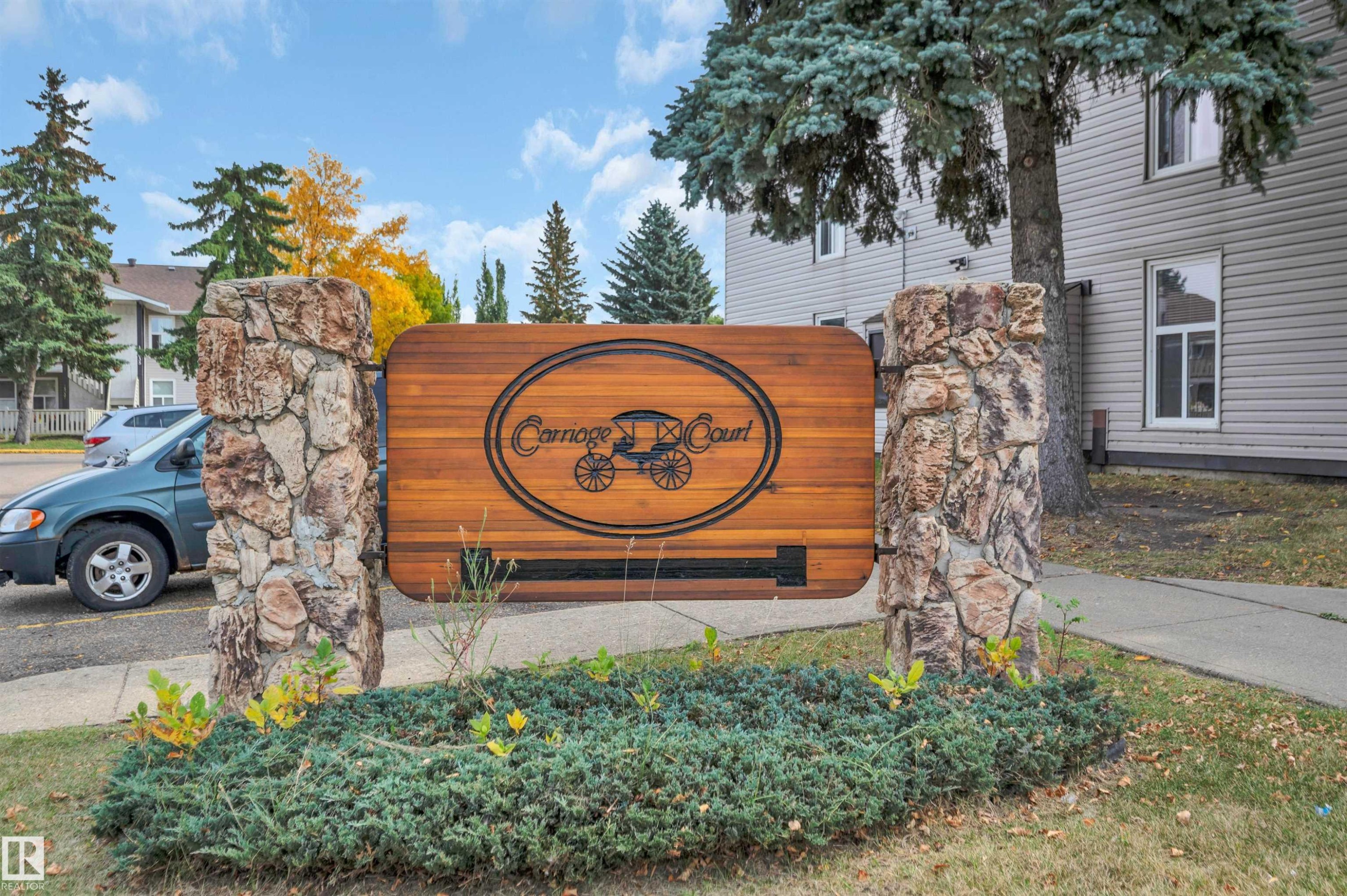 Stone and wood-finish entry sign with established landscaping - 15017 26 Street Nw, Edmonton, AB
