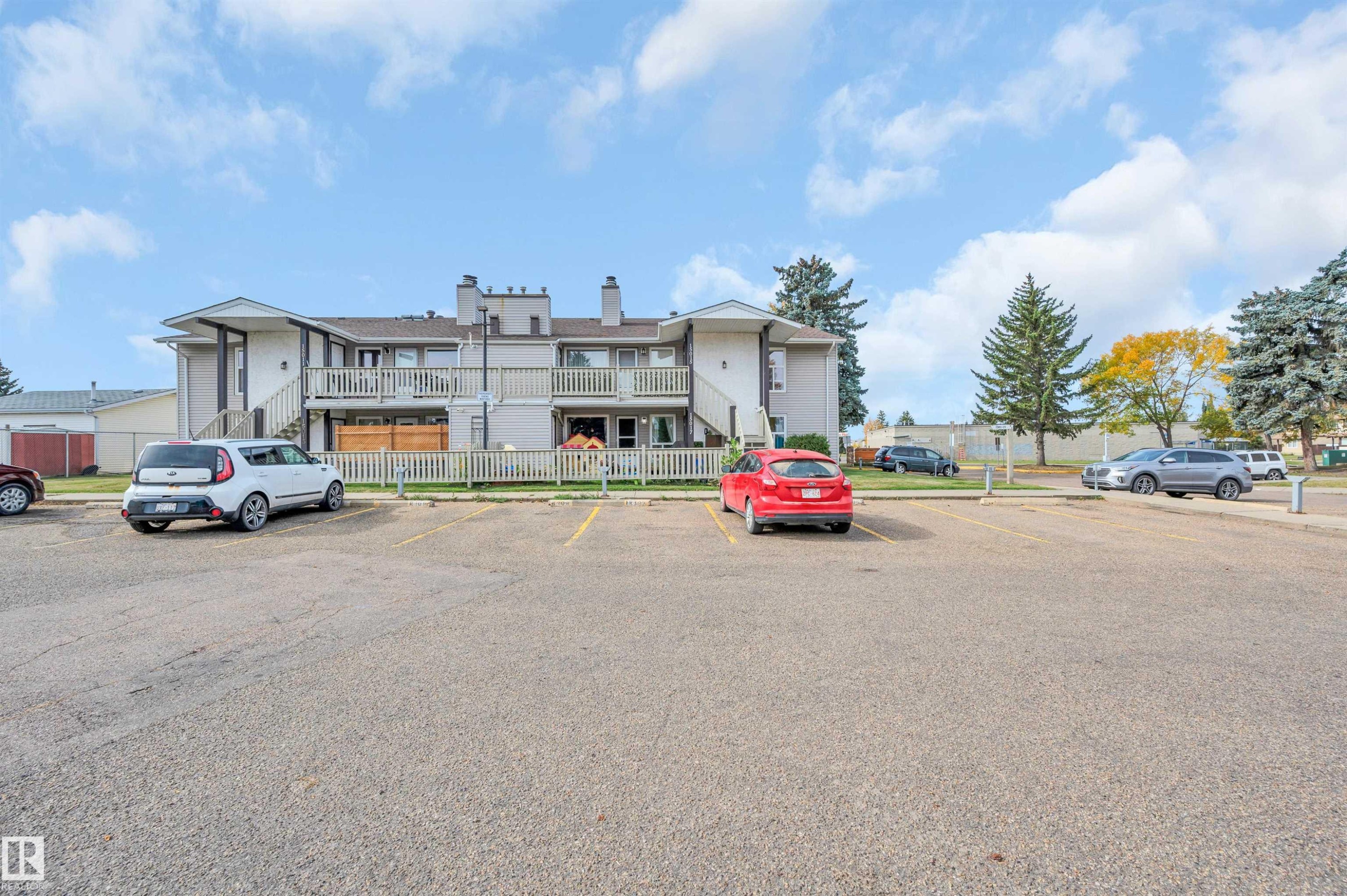 Paved parking lot with designated spaces, featuring mature evergreen trees and deciduous trees - 15017 26 Street Nw, Edmonton, AB