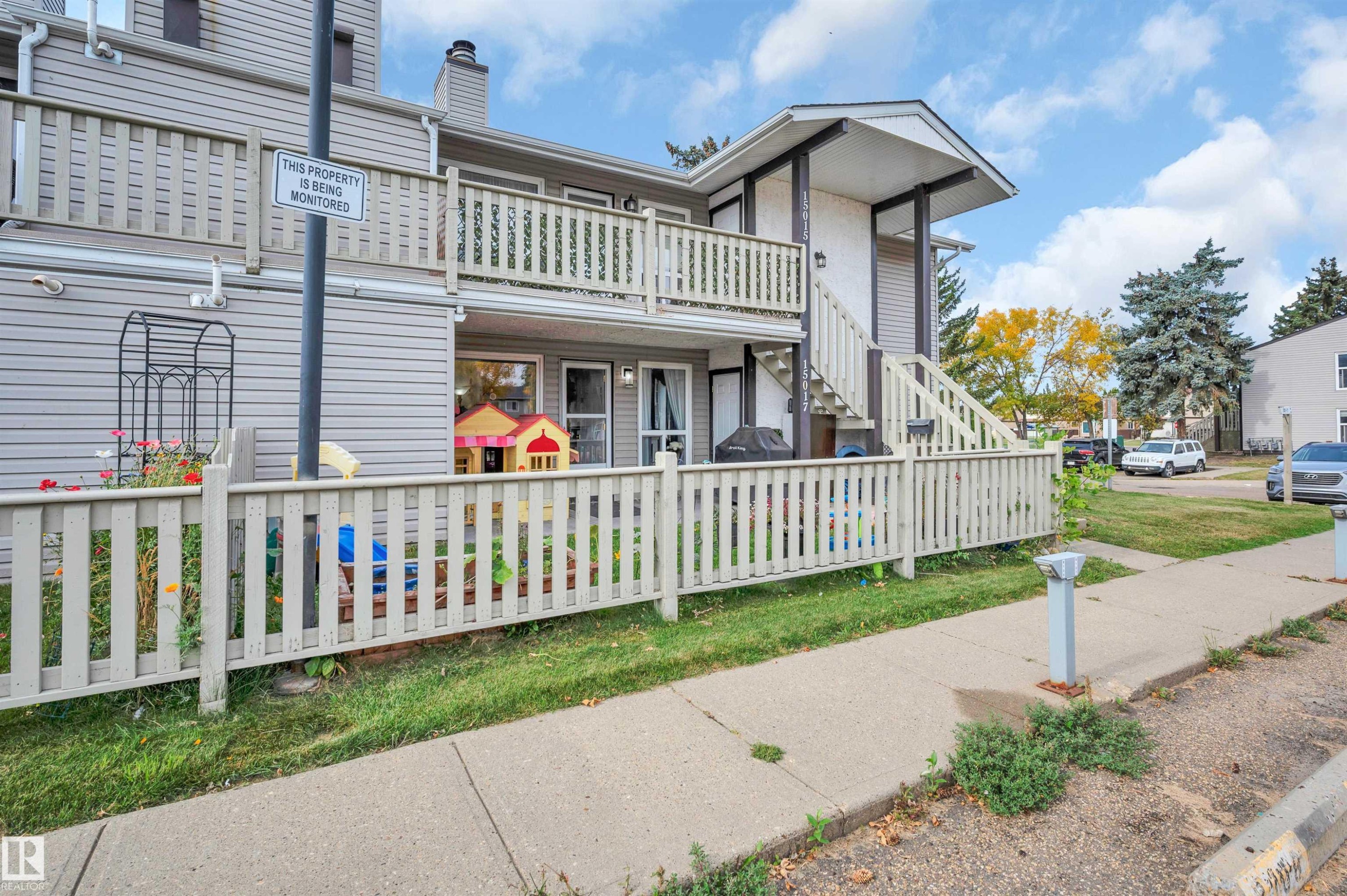 Siding exterior with a white picket fence, concrete sidewalk, and a second-story balcony - 15017 26 Street Nw, Edmonton, AB
