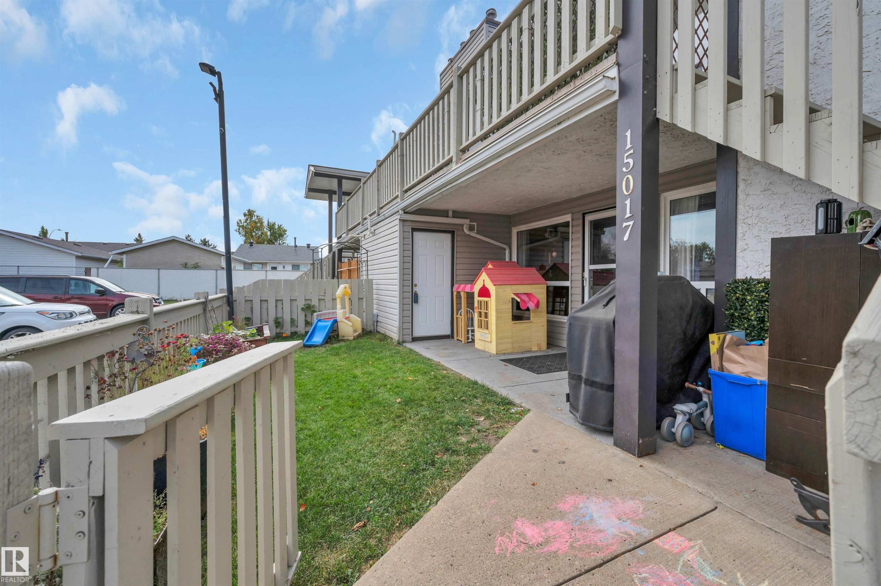 Ground-level patio with concrete flooring, private fenced yard with grass, and an upper-level balcony with wood railing - 15017 26 Street Nw, Edmonton, AB