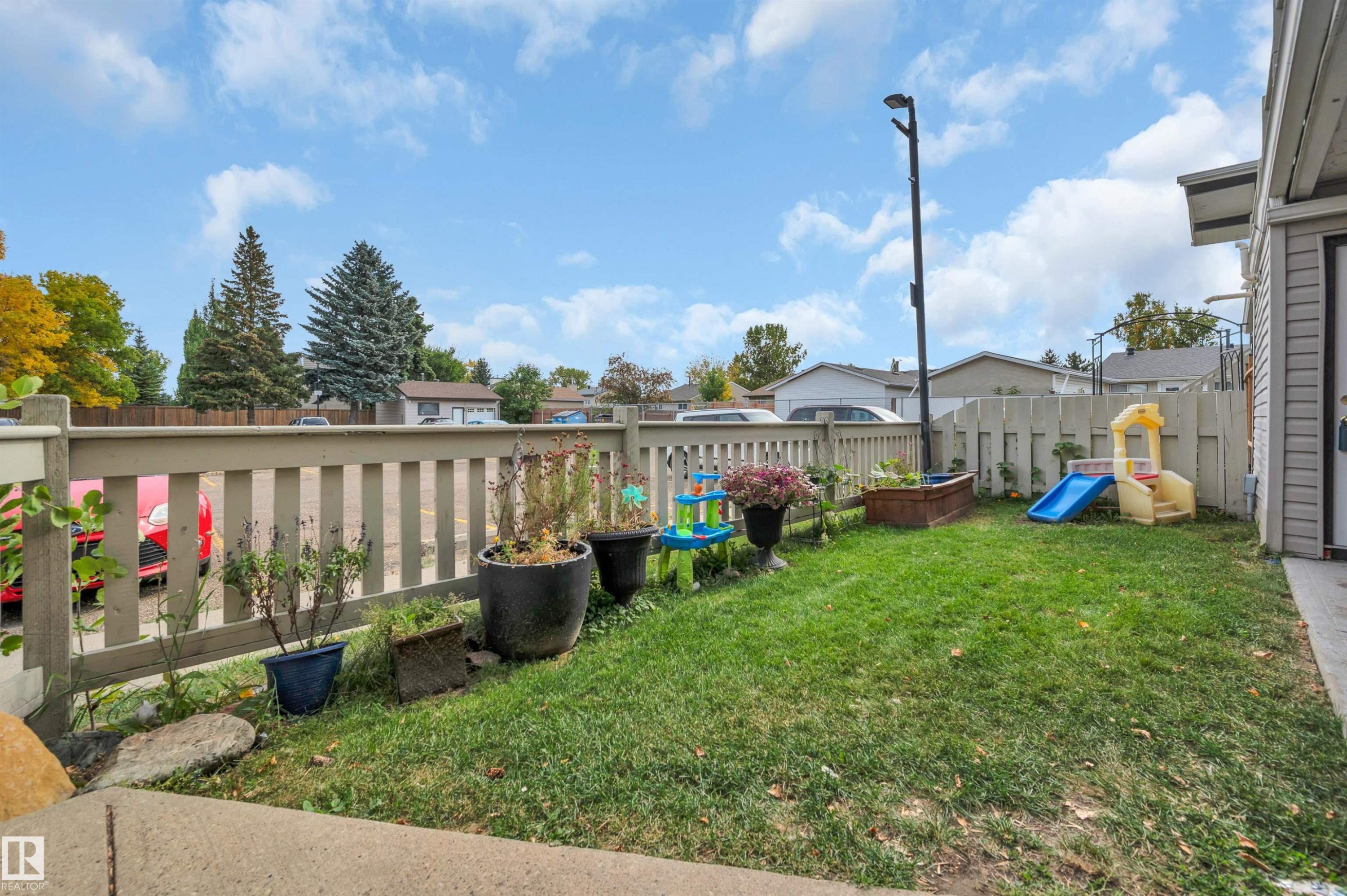 Fenced backyard featuring a manicured lawn, an elevated garden bed, and mature trees - 15017 26 Street Nw, Edmonton, AB