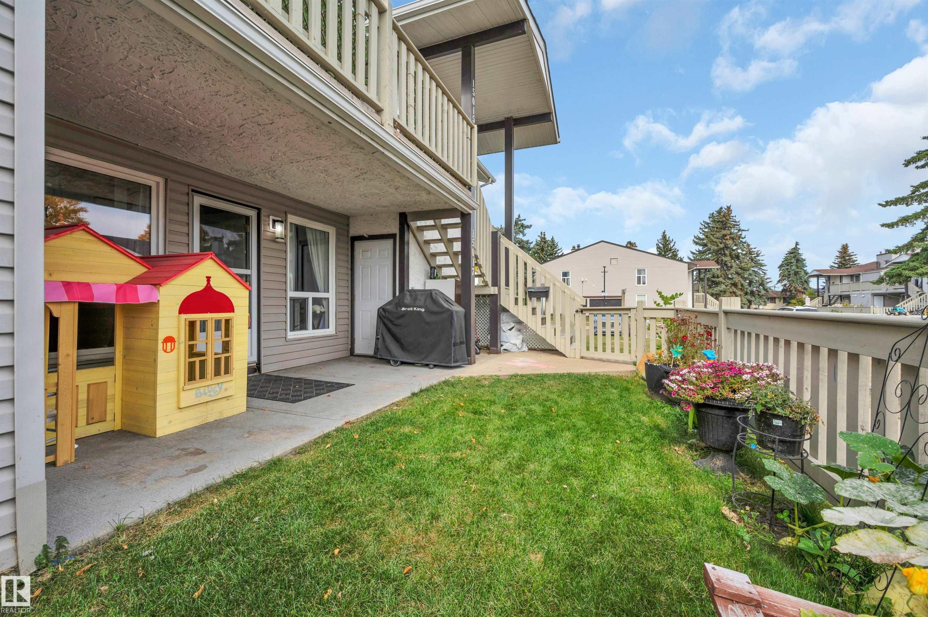 Ground-level patio with concrete surfacing and an expansive grass area - 15017 26 Street Nw, Edmonton, AB