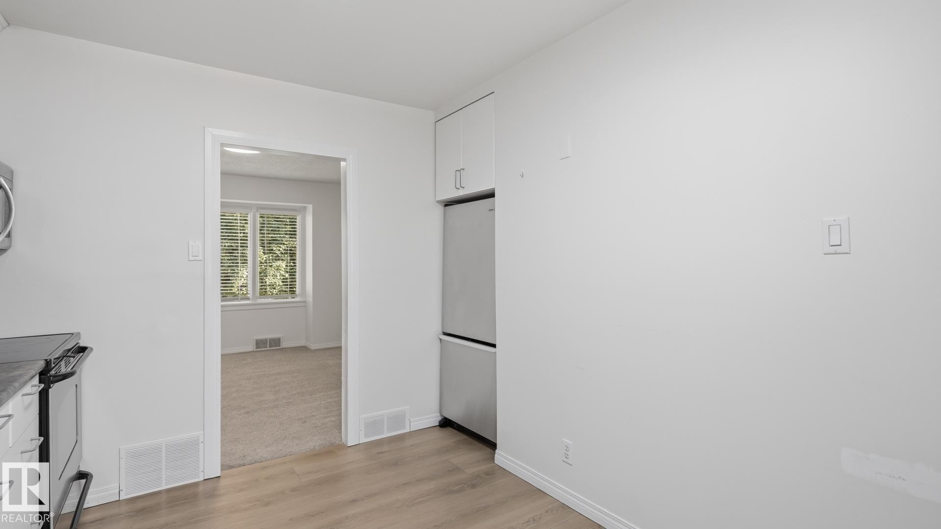 Wood-finish flooring with white baseboards, stainless steel refrigerator, white cabinetry, and a passage to another room - 11836 62 Street Nw, Edmonton, AB