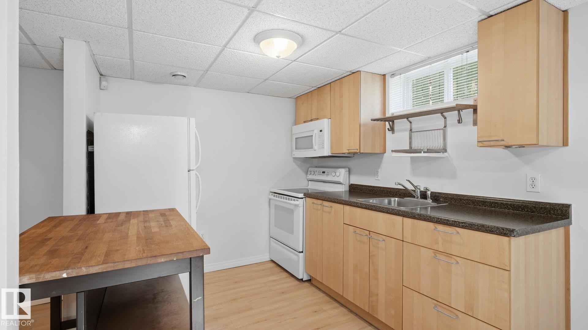 Kitchen featuring wood-finish cabinetry, white appliances, dark countertops, and wood-finish flooring - 11836 62 Street Nw, Edmonton, AB