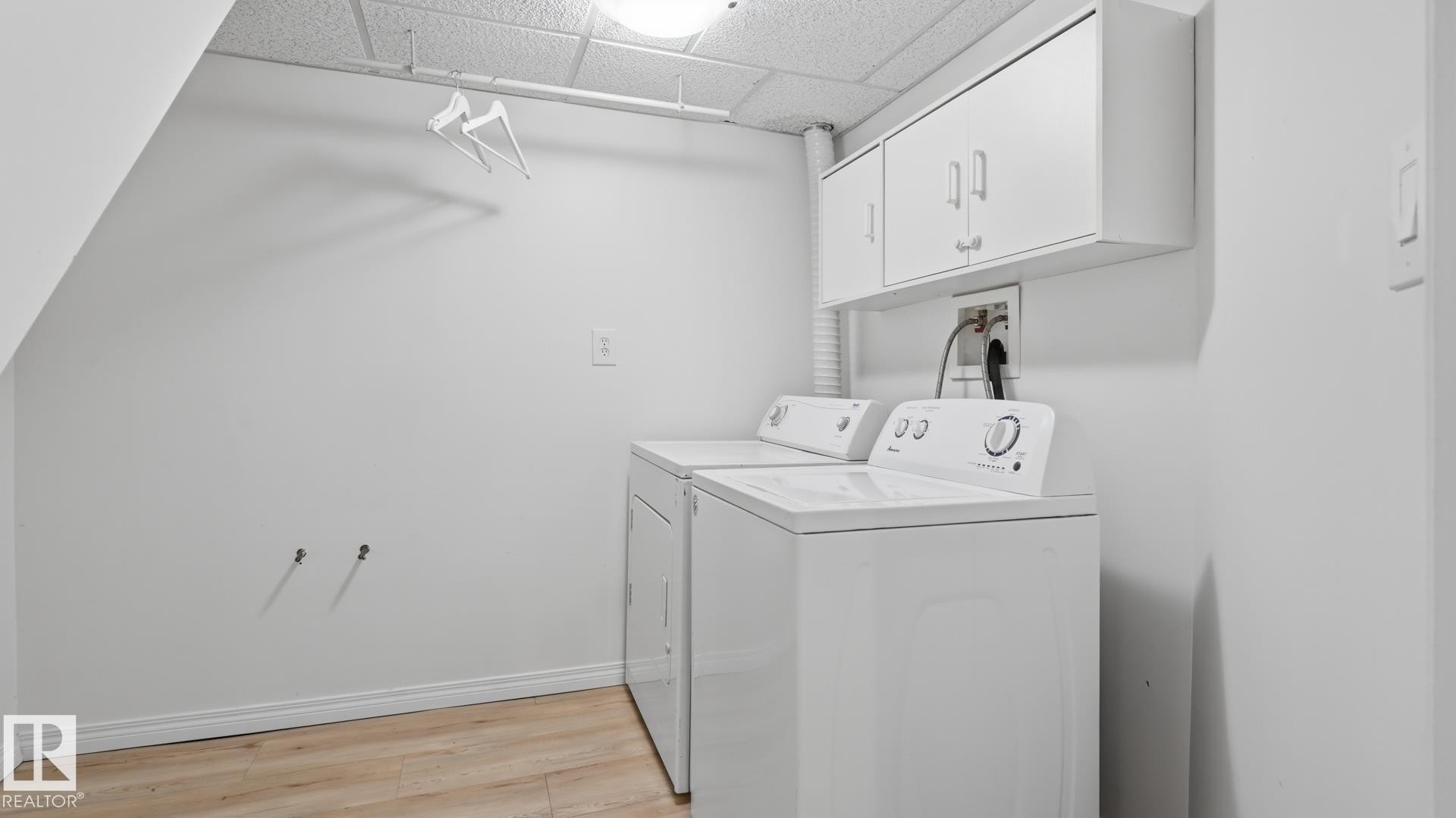 Dedicated laundry area featuring a washer, dryer, wood-finish flooring, and wall-mounted cabinetry - 11836 62 Street Nw, Edmonton, AB