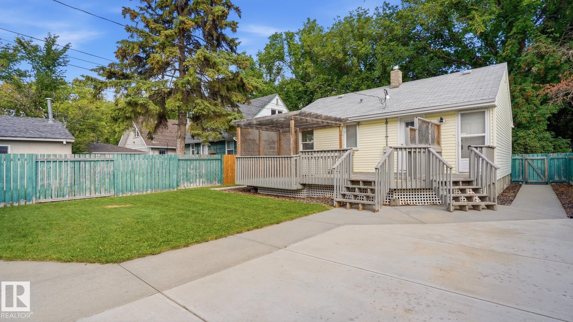 Rear exterior featuring yellow siding, a multi-level wood deck, an attached wood pergola, a concrete patio, and a grass lawn - 11836 62 Street Nw, Edmonton, AB