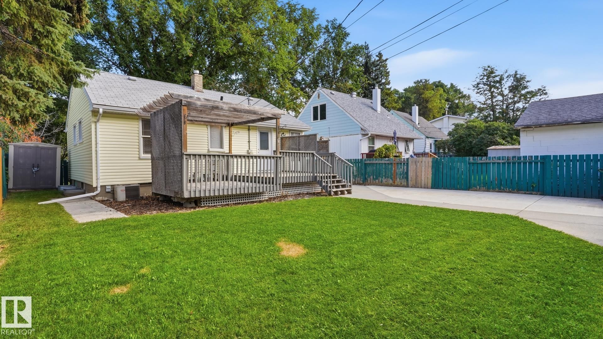 Expansive backyard featuring a manicured lawn, a large wood deck with a pergola, and a paved driveway - 11836 62 Street Nw, Edmonton, AB