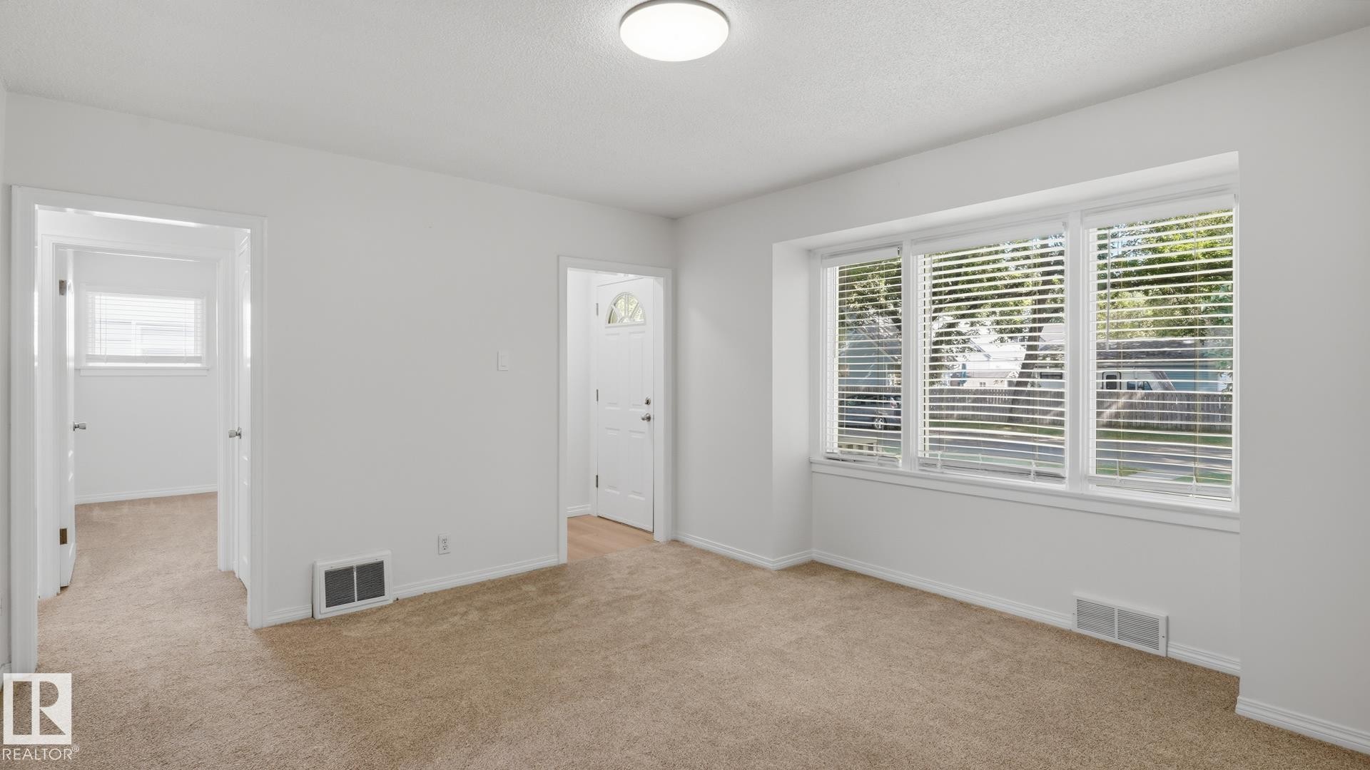 Neutral carpeted flooring, white painted walls, natural light from a multi-pane window, flush-mount ceiling light fixture, and white interior doors - 11836 62 Street Nw, Edmonton, AB