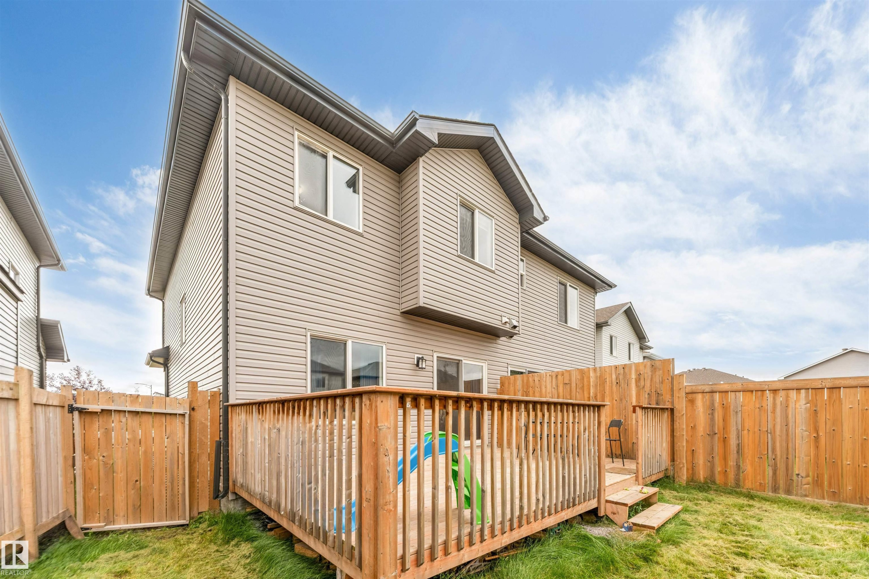 Two-story exterior with siding, featuring a wooden deck with railing, a wooden privacy fence, and a grassy lawn - 2004 15 Avenue Nw, Edmonton, AB