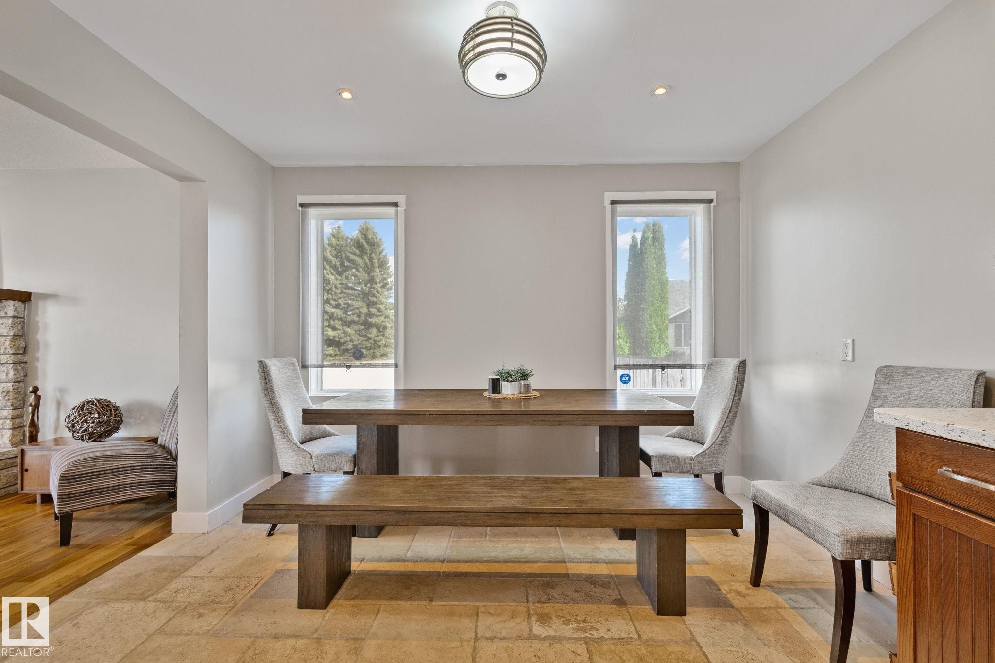 Recessed ceiling lighting, a contemporary drum pendant light, two windows with roller shades, stone-tiled flooring, and a stone-clad fireplace - 12403 29A Avenue Nw, Edmonton, AB