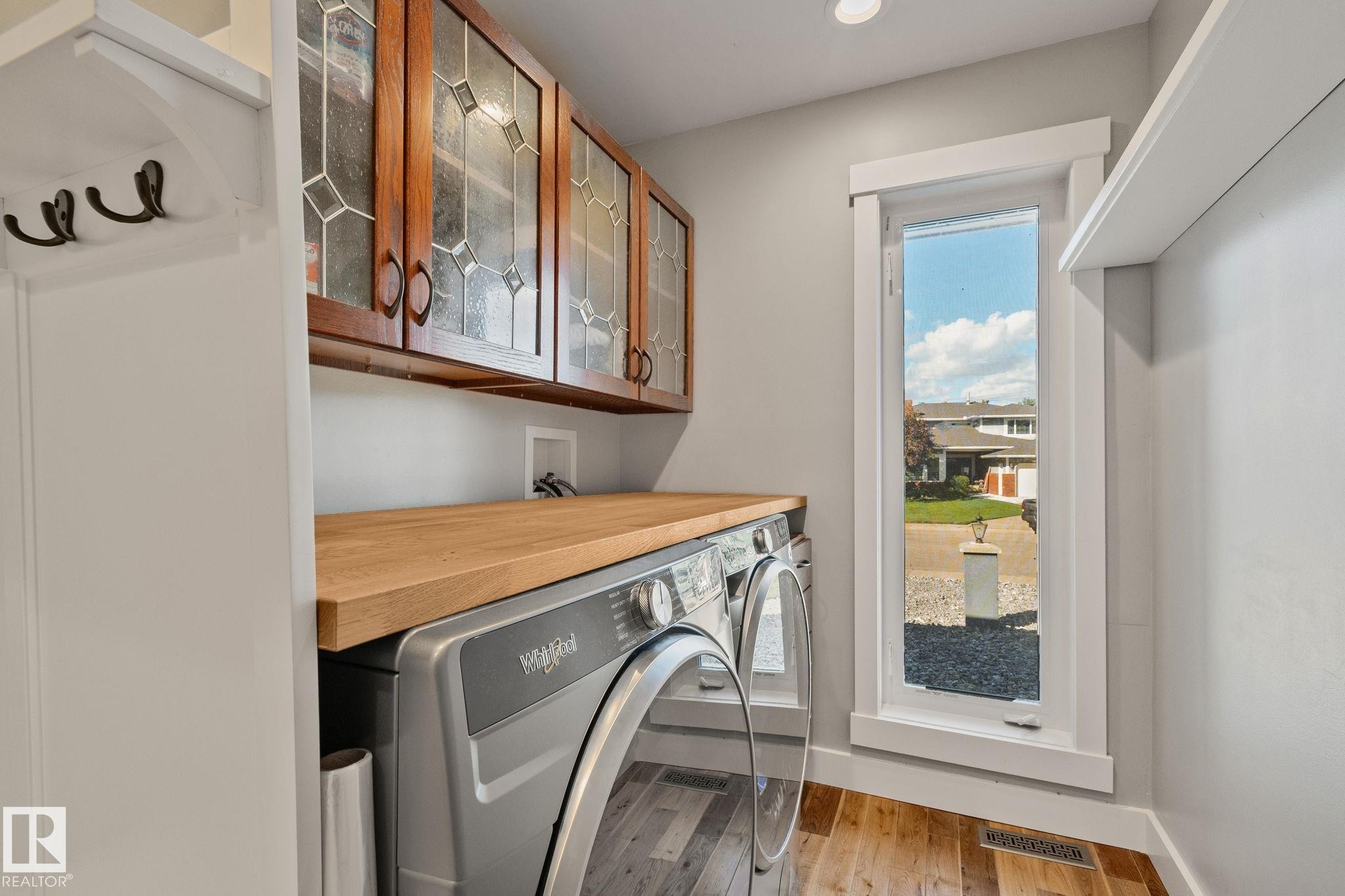 Laundry area with wood-finish flooring, built-in cabinetry featuring leaded glass inserts, a wood countertop, and a vertical window - 12403 29A Avenue Nw, Edmonton, AB